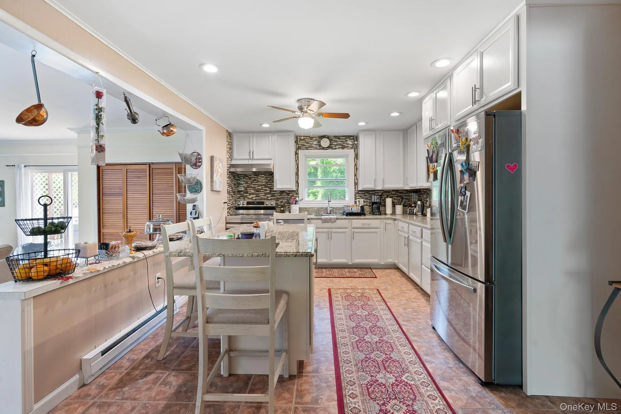 Kitchen featuring stainless steel appliances, a ceiling fan, a baseboard heating unit, decorative backsplash, and white cabinetry Kitchen featuring stainless steel appliances, a ceiling fan, a baseboard heating unit, decorative backsplash, and white cabinetry