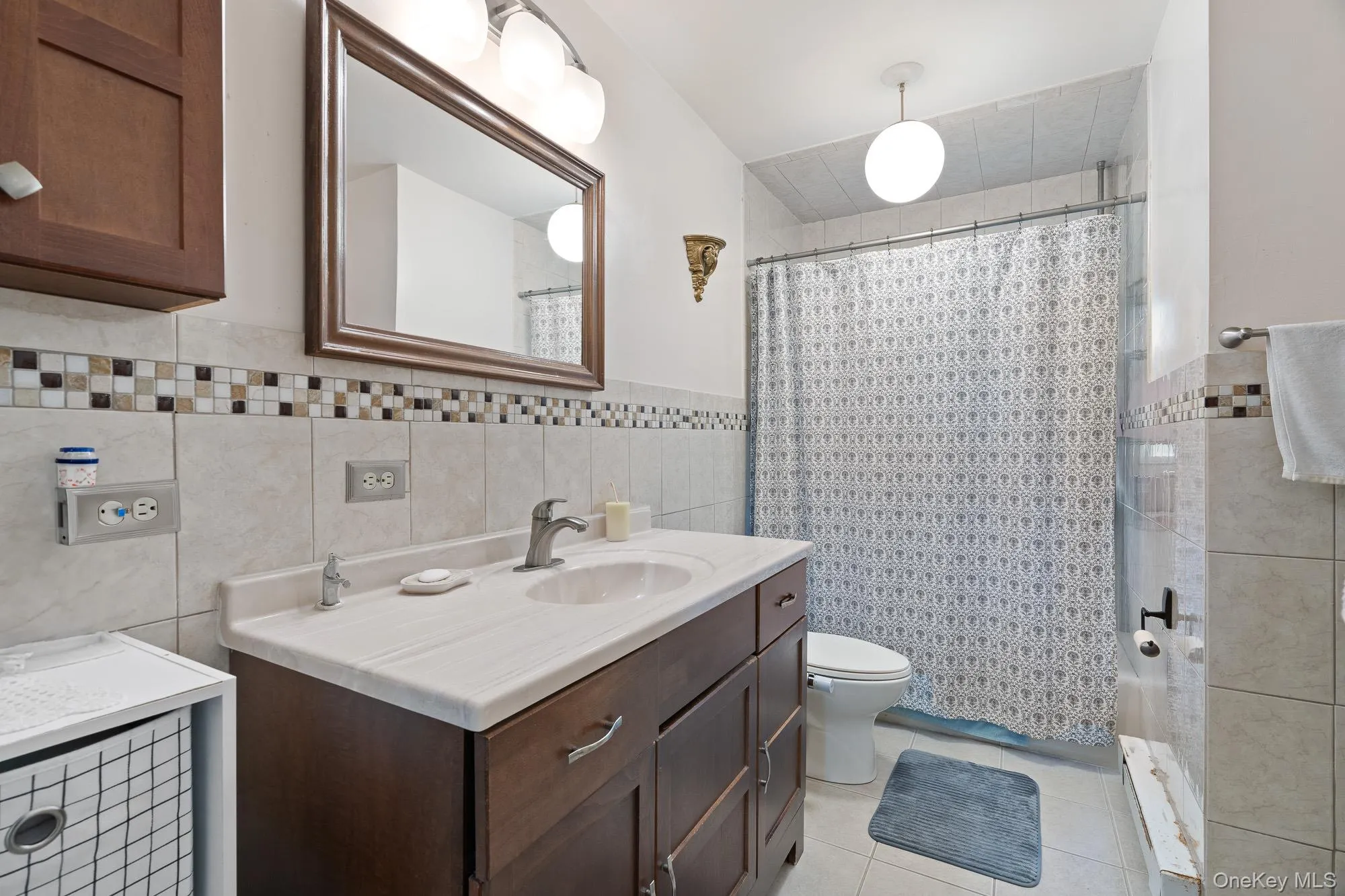 Bathroom with tile walls, vanity, tile patterned flooring, toilet, and curtained shower Bathroom with tile walls, vanity, tile patterned flooring, toilet, and curtained shower
