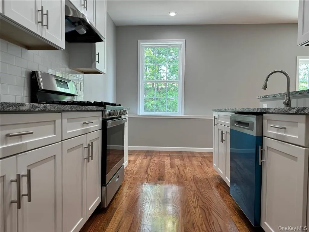 Kitchen featuring dishwashing machine, stainless steel range with gas cooktop, white cabinets, decorative backsplash, and dark hardwood / wood-style floors Kitchen featuring dishwashing machine, stainless steel range with gas cooktop, white cabinets, decorative backsplash, and dark hardwood / wood-style floors