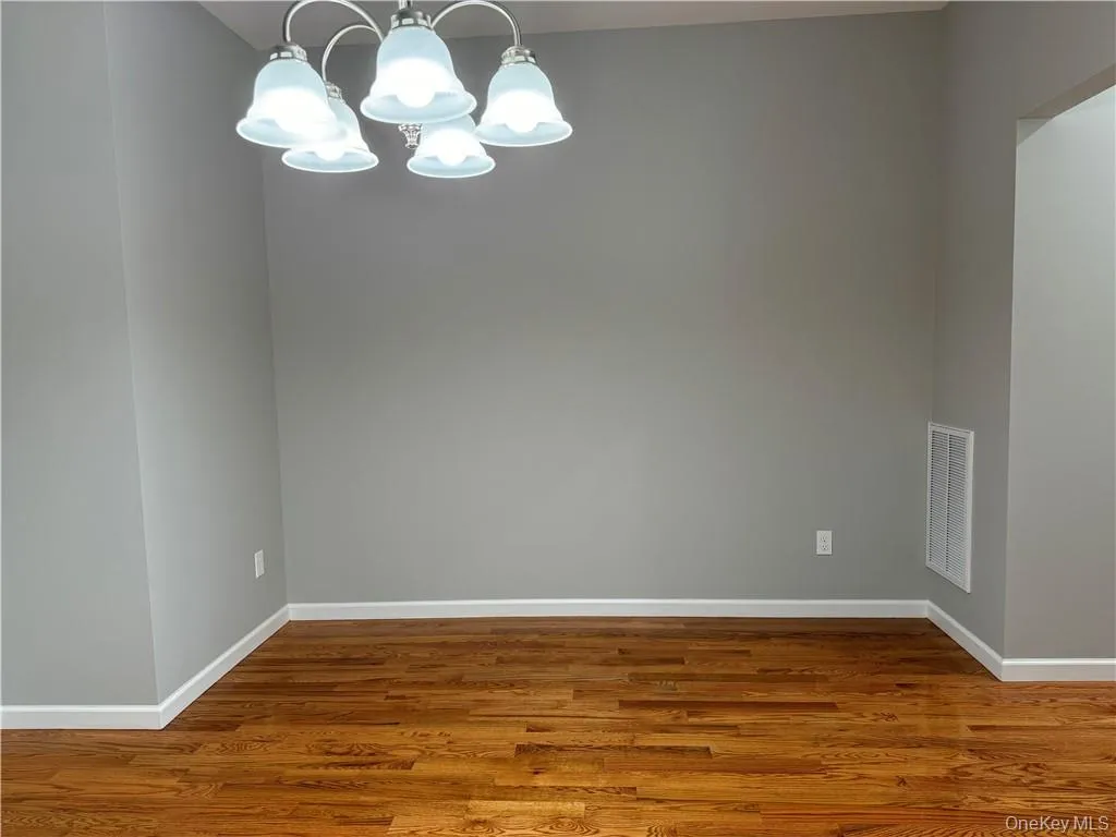Spare room featuring a notable chandelier and hardwood / wood-style floors Spare room featuring a notable chandelier and hardwood / wood-style floors