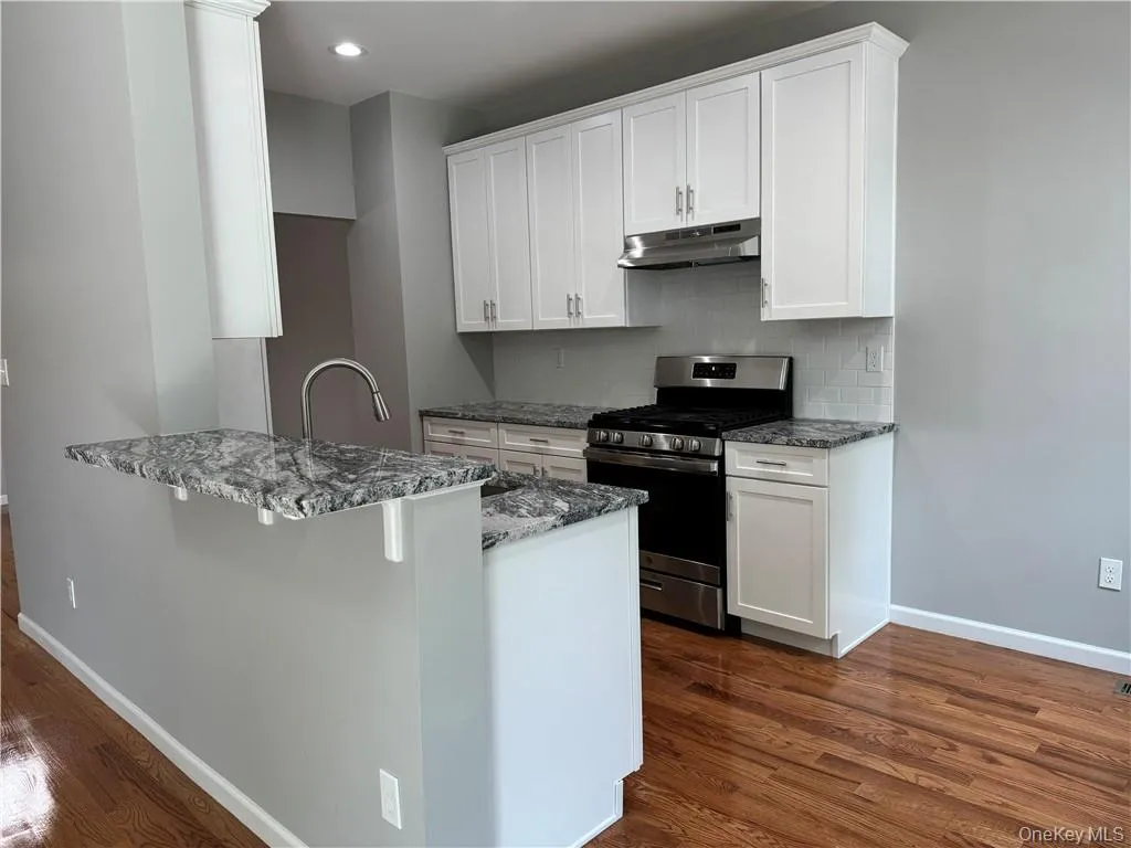 Kitchen with white cabinetry, stainless steel gas range oven, and dark hardwood / wood-style flooring Kitchen with white cabinetry, stainless steel gas range oven, and dark hardwood / wood-style flooring