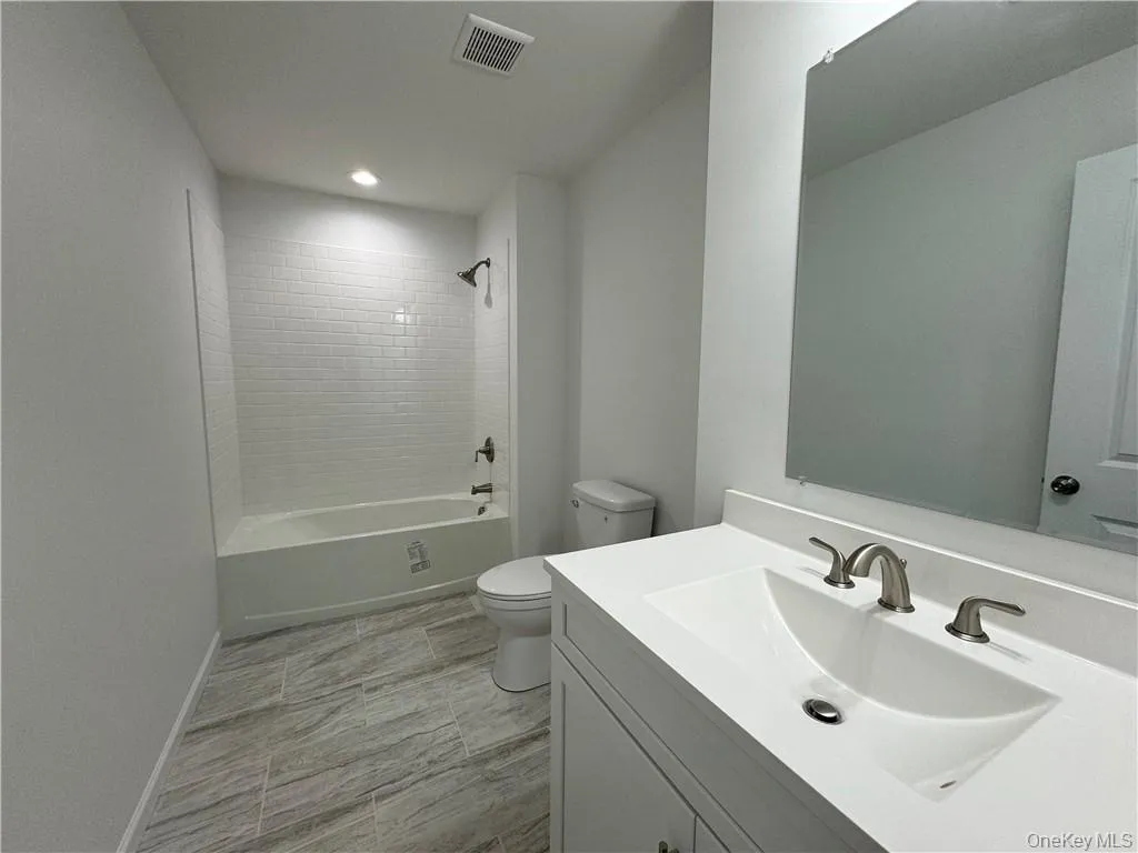 Full bathroom with vanity, toilet, tile patterned floors, and tiled shower / bath Full bathroom with vanity, toilet, tile patterned floors, and tiled shower / bath