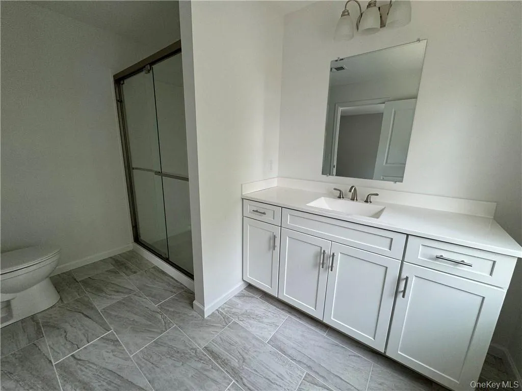 Bathroom featuring a shower with door, vanity, toilet, and tile patterned floors Bathroom featuring a shower with door, vanity, toilet, and tile patterned floors
