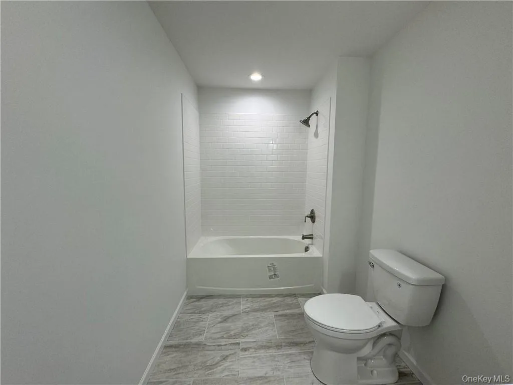 Bathroom with tiled shower / bath combo, tile patterned floors, and toilet Bathroom with tiled shower / bath combo, tile patterned floors, and toilet