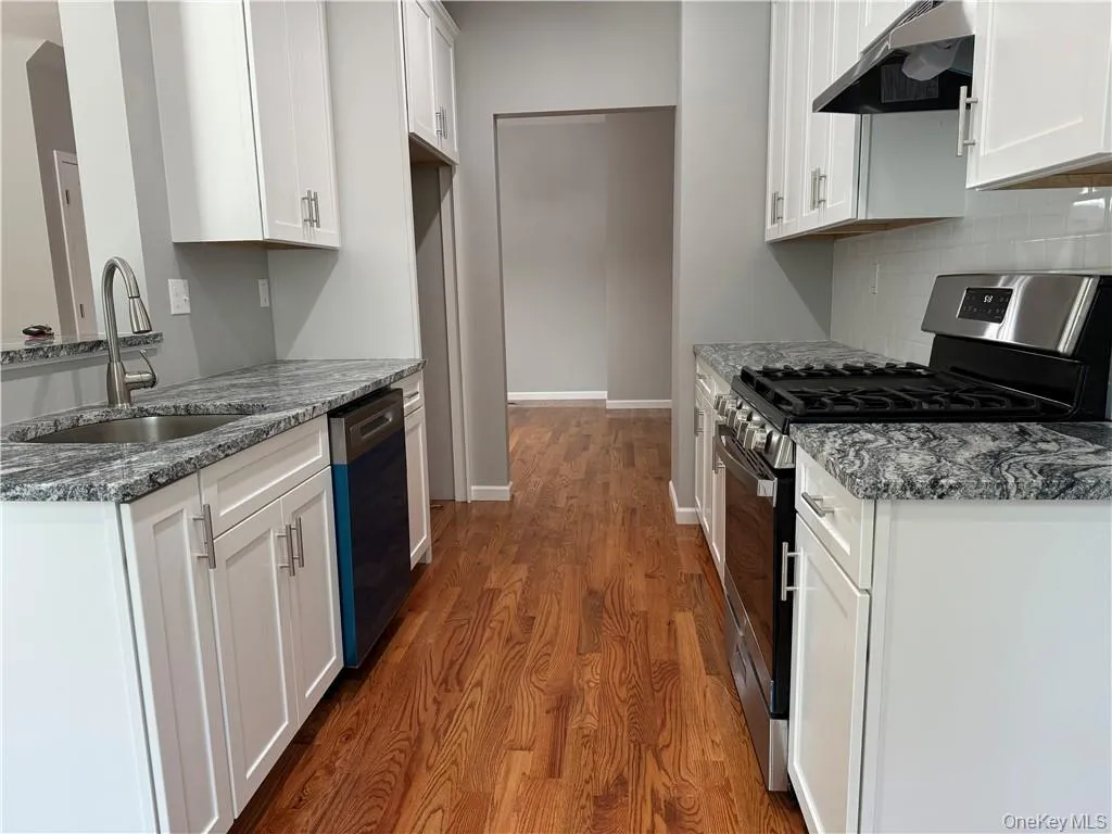 Kitchen with gas range, white cabinetry, dark hardwood / wood-style flooring, dishwasher, and backsplash Kitchen with gas range, white cabinetry, dark hardwood / wood-style flooring, dishwasher, and backsplash
