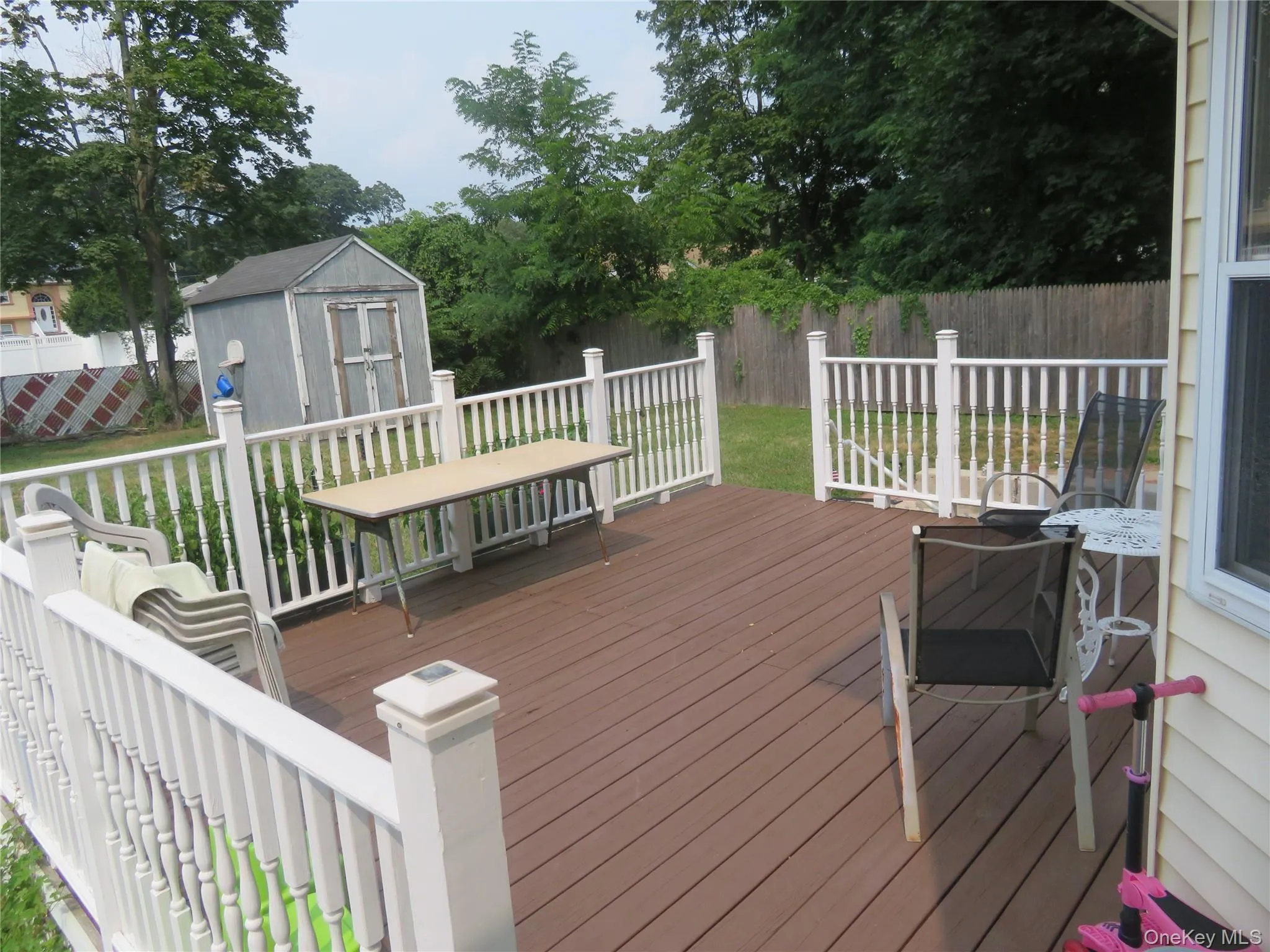 Expansive outdoor deck featuring wood-finish flooring, white railing, and a storage shed Expansive outdoor deck featuring wood-finish flooring, white railing, and a storage shed