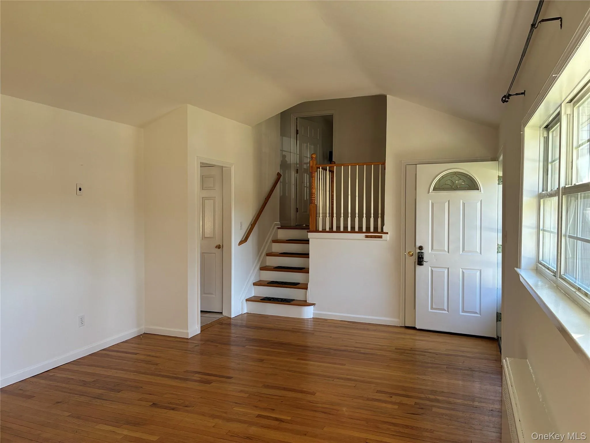 Hardwood flooring, paneled entry door with an arched glass insert, multi-pane windows, and a staircase with a wood handrail Hardwood flooring, paneled entry door with an arched glass insert, multi-pane windows, and a staircase with a wood handrail