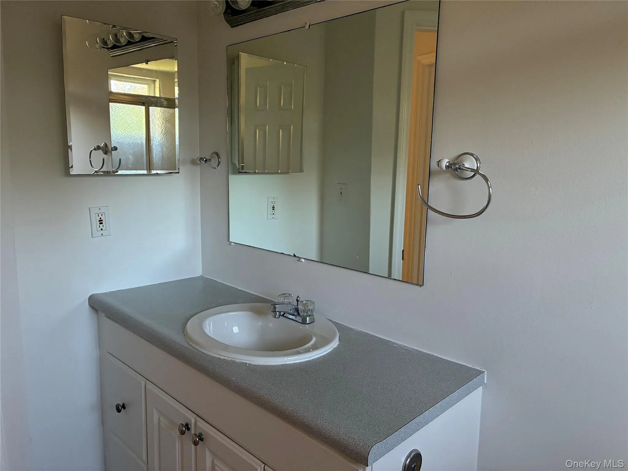 Recessed sink with chrome faucet, white vanity cabinetry, gray countertop, and overhead mirror Recessed sink with chrome faucet, white vanity cabinetry, gray countertop, and overhead mirror