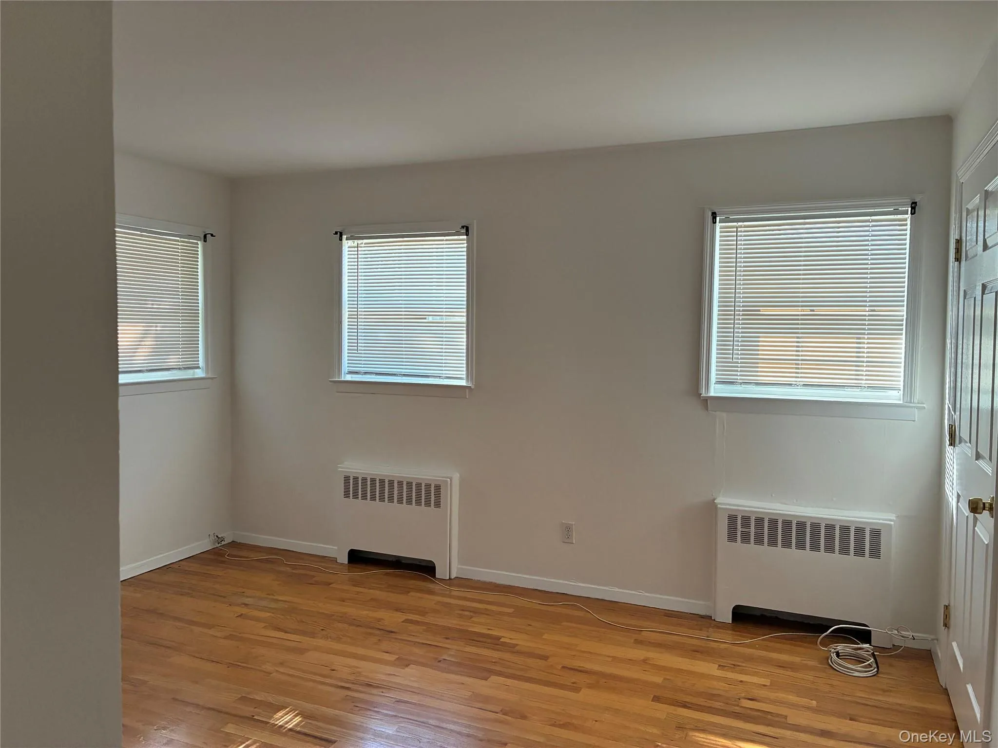 Hardwood flooring throughout, multiple windows, white painted walls, and a paneled door Hardwood flooring throughout, multiple windows, white painted walls, and a paneled door