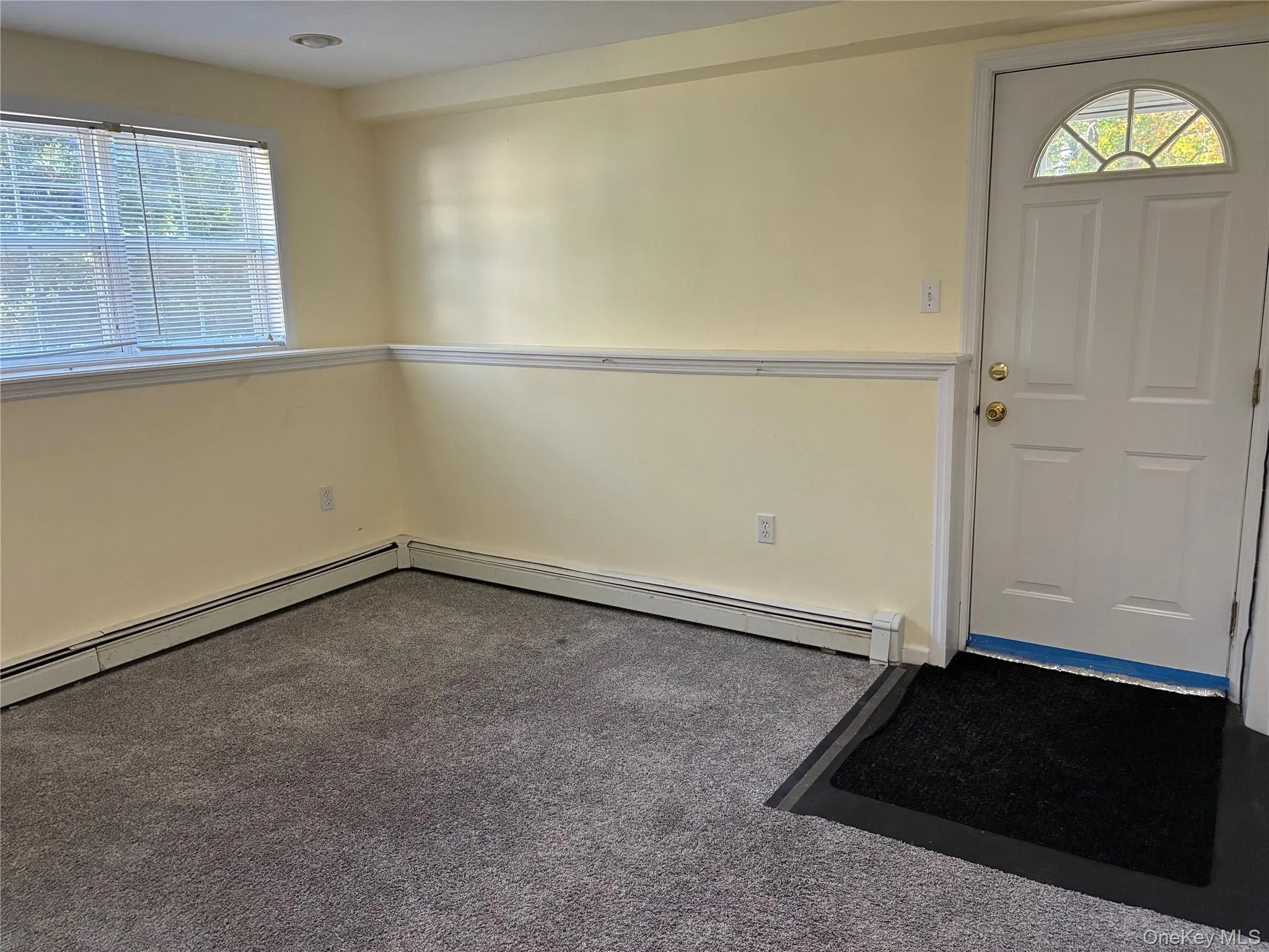 Outside entrance. Carpeted room featuring a white paneled door with an arched glass insert, a window with blinds, and baseboard heating Outside entrance. Carpeted room featuring a white paneled door with an arched glass insert, a window with blinds, and baseboard heating