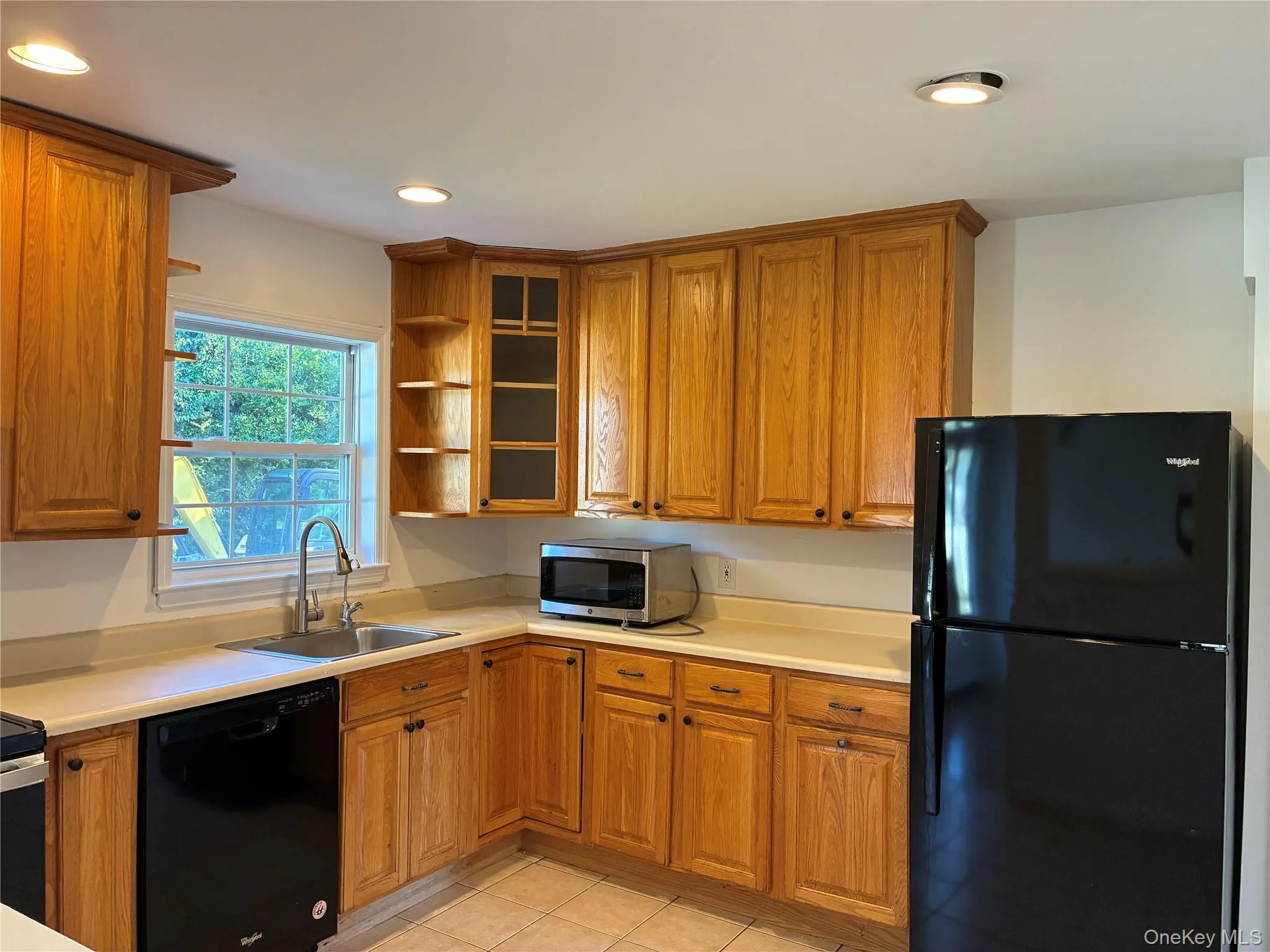 Kitchen featuring wood cabinetry, solid surface countertops, stainless steel sink, black appliances, and recessed lighting Kitchen featuring wood cabinetry, solid surface countertops, stainless steel sink, black appliances, and recessed lighting