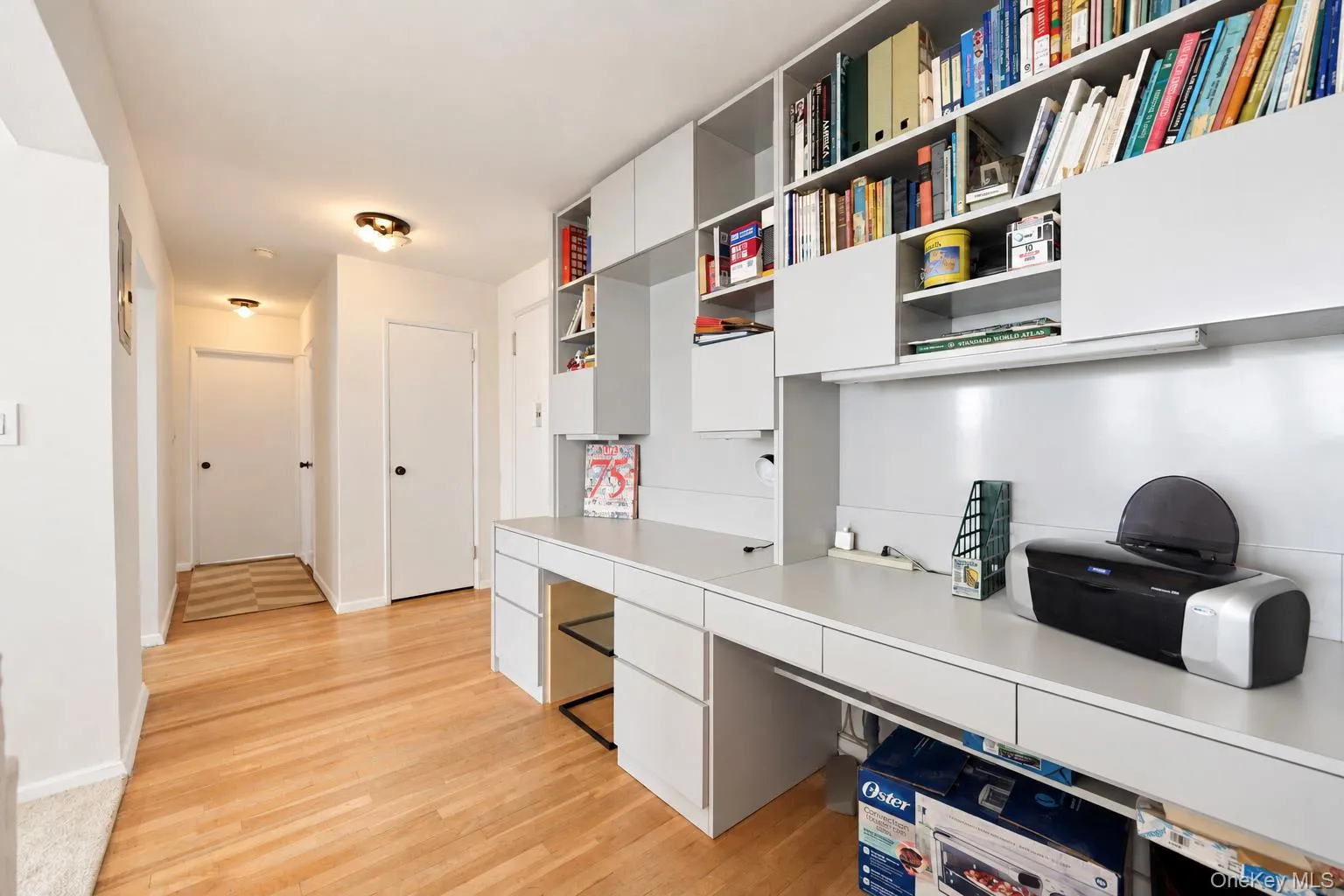 Integrated built-in desk with overhead shelving and cabinetry, wood-finish flooring, and flush-mount ceiling lighting Integrated built-in desk with overhead shelving and cabinetry, wood-finish flooring, and flush-mount ceiling lighting