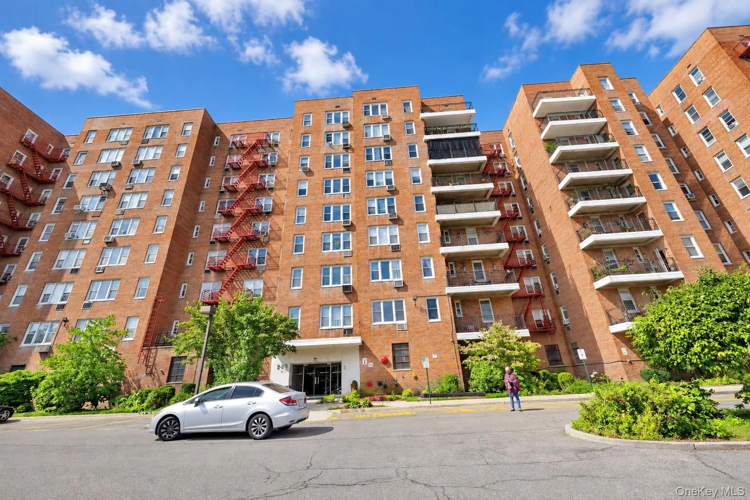 Multi-story brick facade building featuring numerous windows, multiple balconies with railings, and established landscaping Multi-story brick facade building featuring numerous windows, multiple balconies with railings, and established landscaping