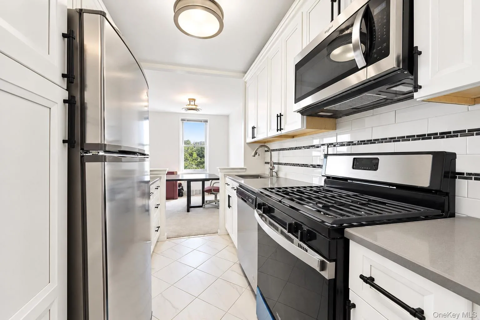 Stainless steel appliances, white cabinetry with black hardware, subway tile backsplash with accent border, and light-toned countertops Stainless steel appliances, white cabinetry with black hardware, subway tile backsplash with accent border, and light-toned countertops