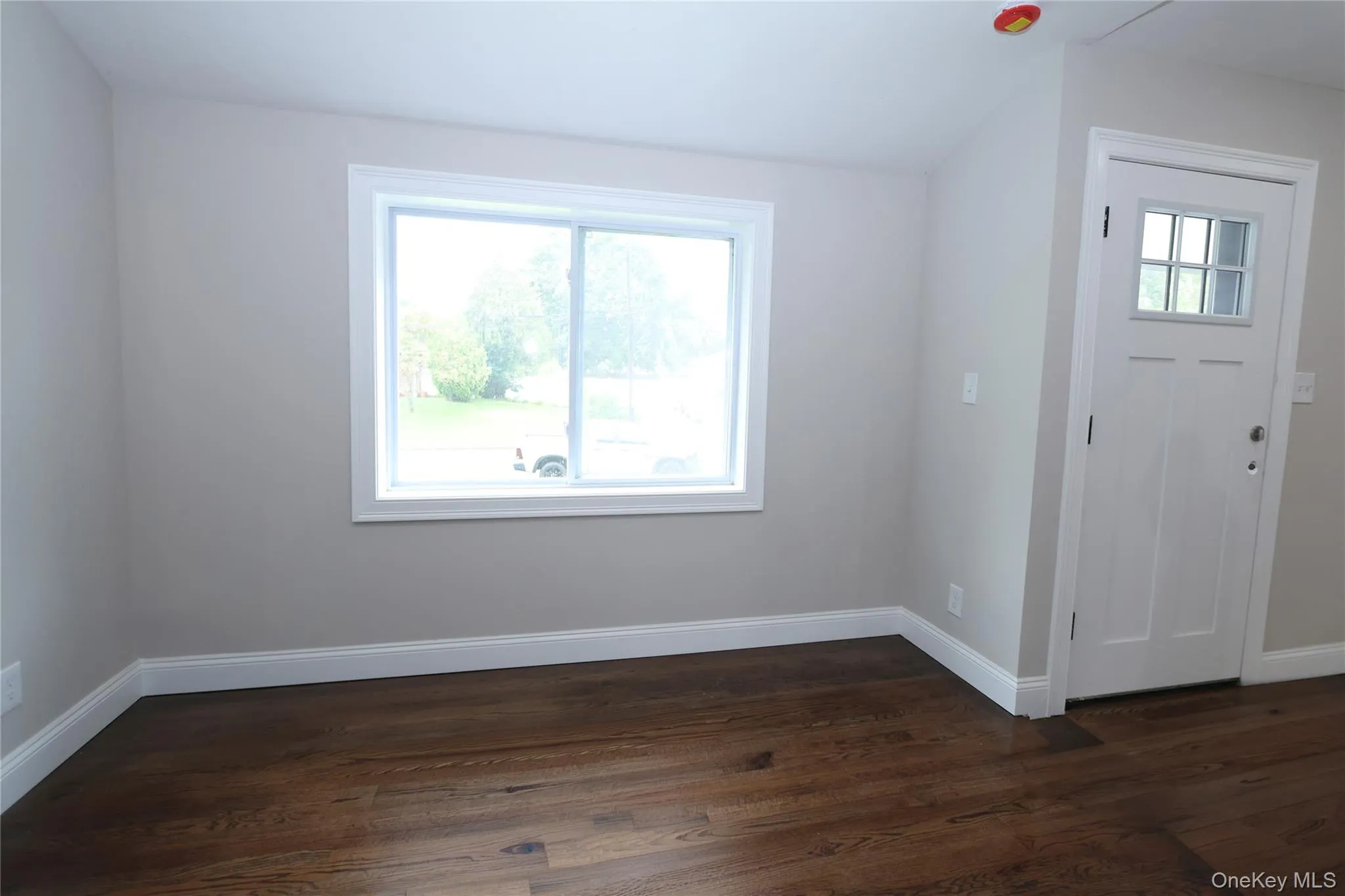 Wood-finish flooring, white trim, and a window with white casing Wood-finish flooring, white trim, and a window with white casing