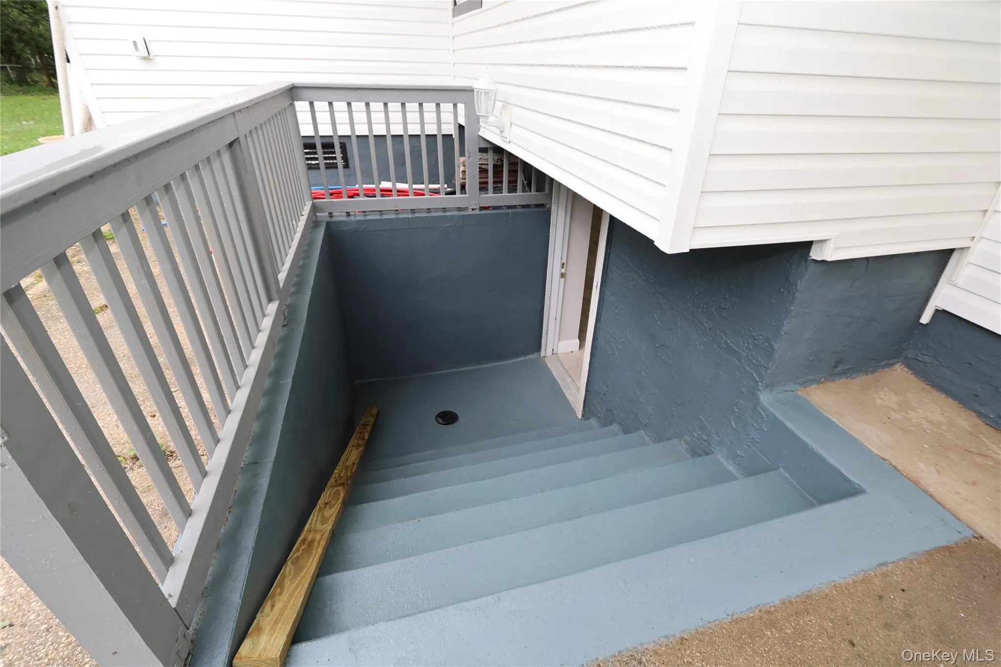Outdoor stairwell featuring painted concrete steps, white vinyl siding, and a wood railing Outdoor stairwell featuring painted concrete steps, white vinyl siding, and a wood railing