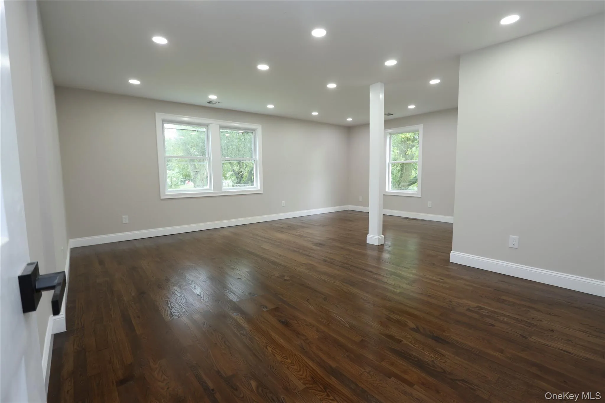 Expansive room with dark wood-finish flooring, recessed lighting, and multiple windows Expansive room with dark wood-finish flooring, recessed lighting, and multiple windows