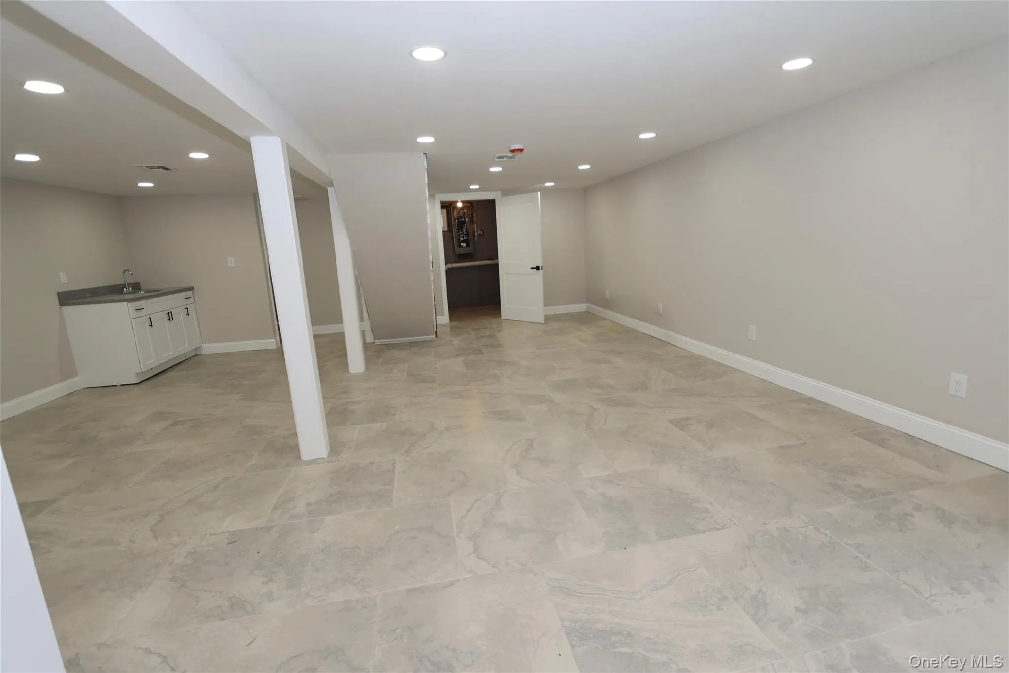 Spacious room with light-toned tile flooring, recessed lighting, and a built-in wet bar featuring white cabinetry and a dark countertop Spacious room with light-toned tile flooring, recessed lighting, and a built-in wet bar featuring white cabinetry and a dark countertop