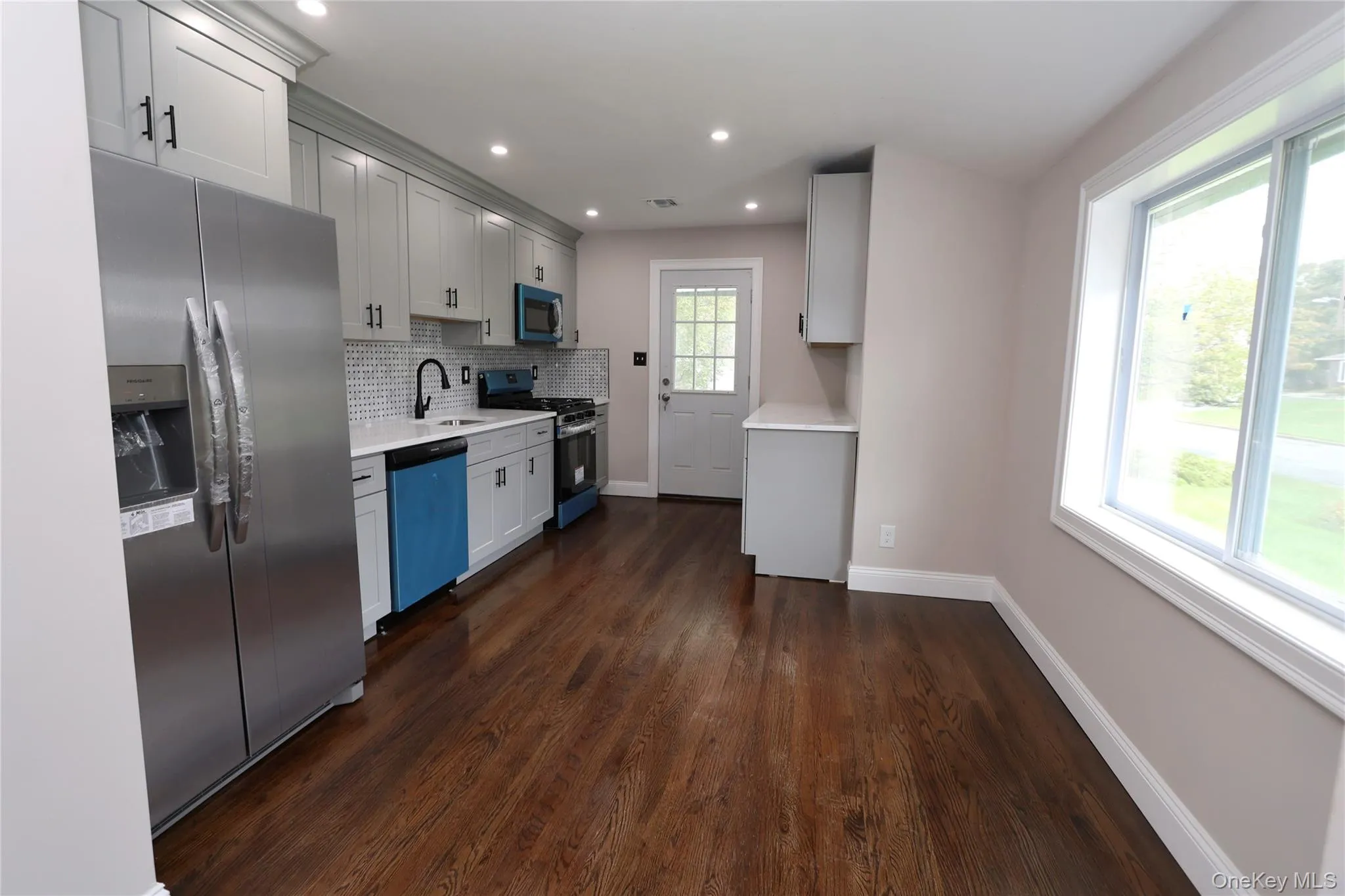 Kitchen featuring wood-finish flooring, recessed lighting, white shaker-style cabinetry, stainless steel appliances, and a tiled backsplash Kitchen featuring wood-finish flooring, recessed lighting, white shaker-style cabinetry, stainless steel appliances, and a tiled backsplash