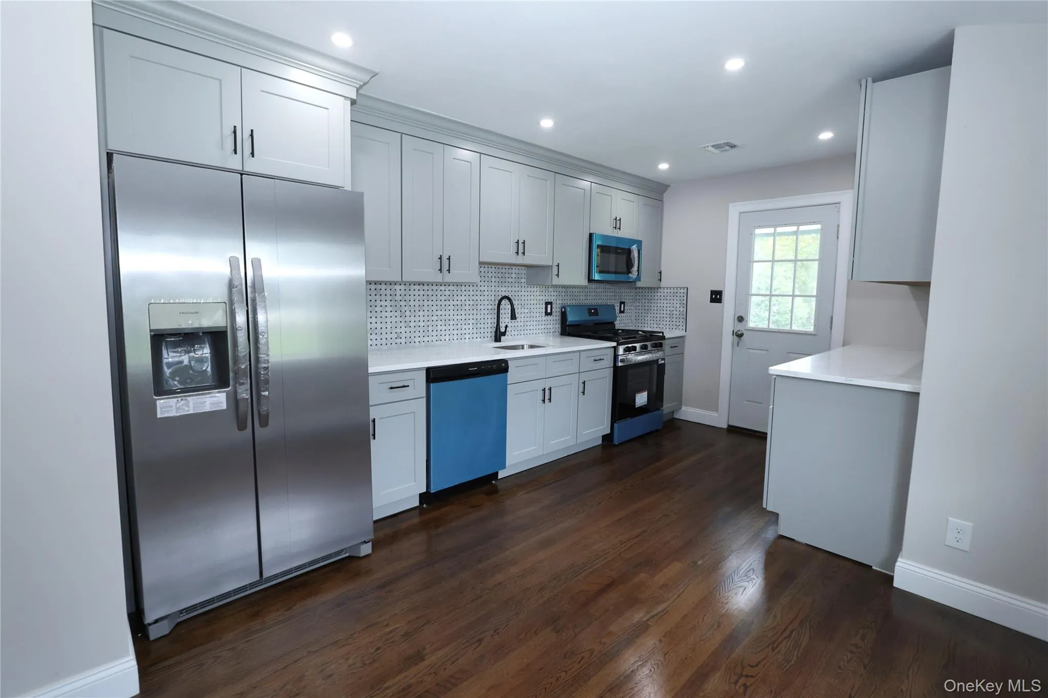 Kitchen featuring wood-finish flooring, light-toned cabinetry, light-toned countertops, a tile backsplash, and recessed lighting Kitchen featuring wood-finish flooring, light-toned cabinetry, light-toned countertops, a tile backsplash, and recessed lighting