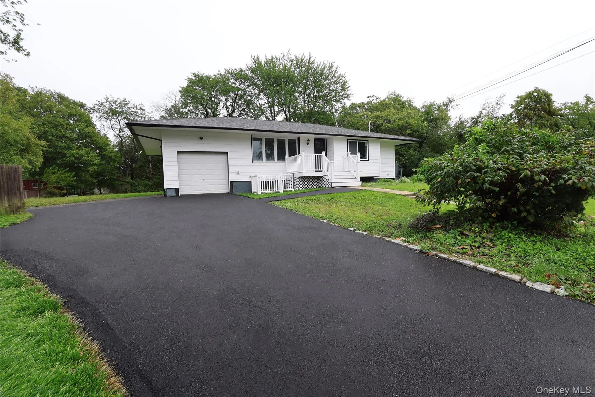White siding exterior with a prominent asphalt driveway, attached garage, and front porch White siding exterior with a prominent asphalt driveway, attached garage, and front porch