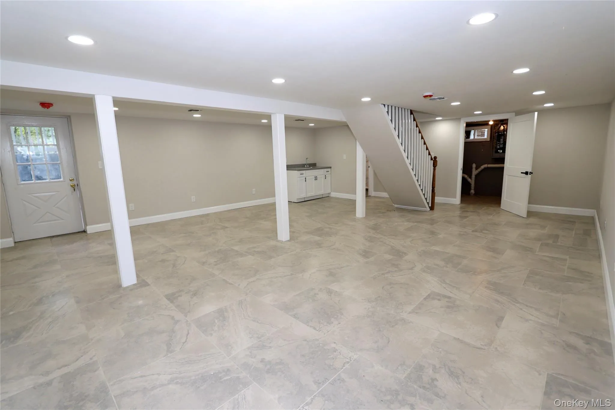 Spacious finished basement featuring recessed lighting, light-toned tile flooring, a built-in wet bar, and a painted wood staircase with a wood handrail Spacious finished basement featuring recessed lighting, light-toned tile flooring, a built-in wet bar, and a painted wood staircase with a wood handrail