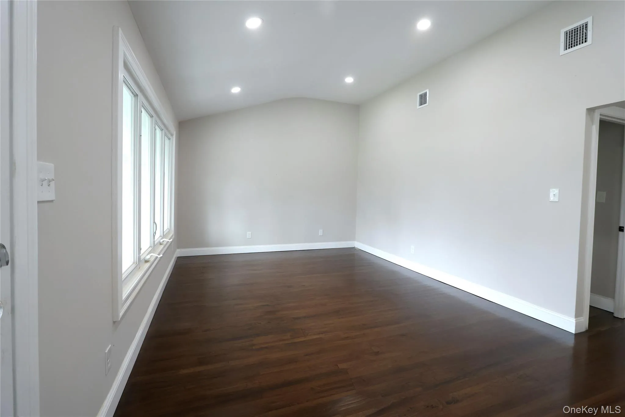 Vaulted ceiling with recessed lighting, dark wood-finish flooring, multiple windows, and white baseboards Vaulted ceiling with recessed lighting, dark wood-finish flooring, multiple windows, and white baseboards