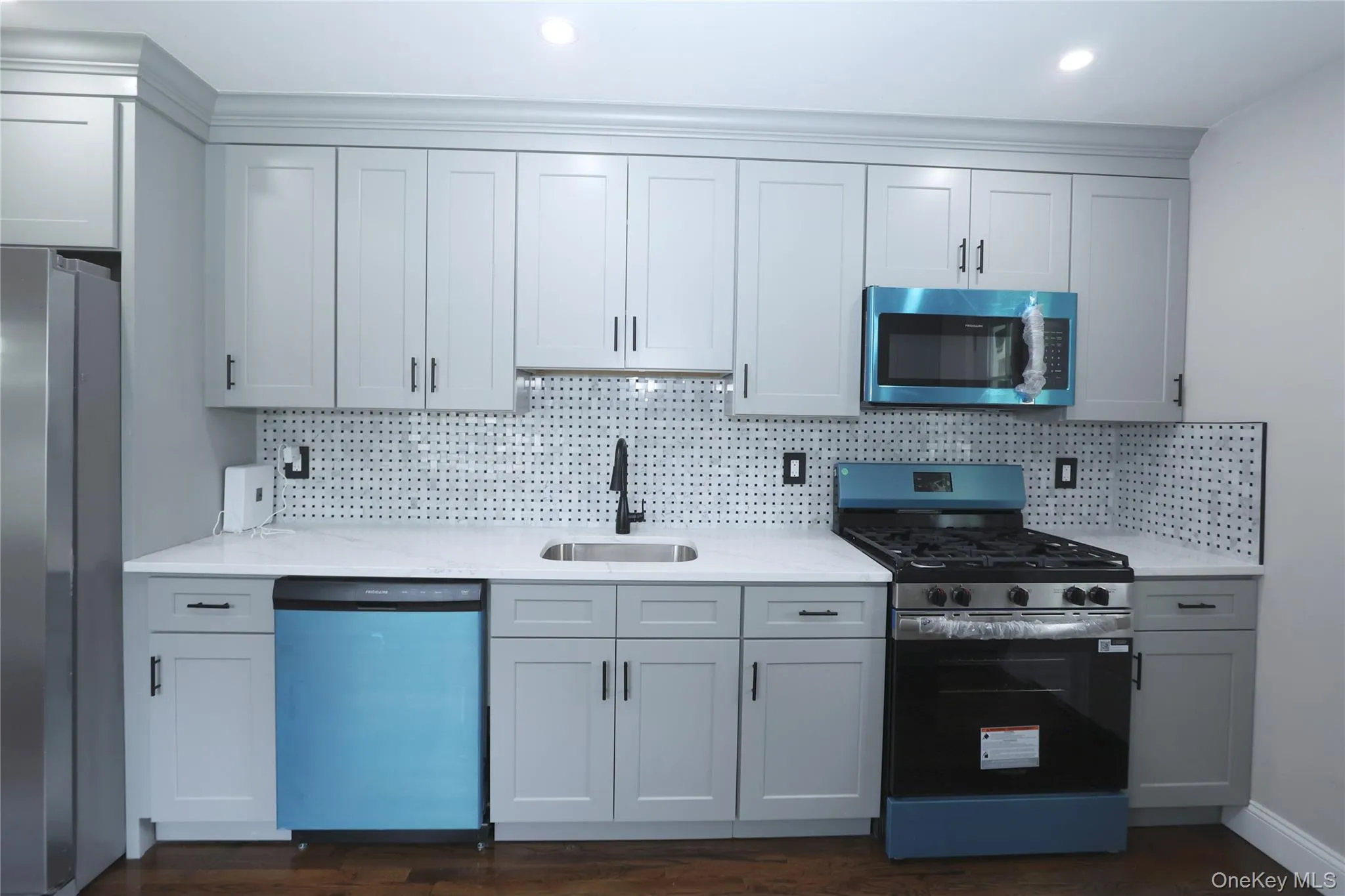 Updated kitchen featuring light gray cabinetry, white countertops, stainless steel appliances, a gas range, and a patterned tile backsplash Updated kitchen featuring light gray cabinetry, white countertops, stainless steel appliances, a gas range, and a patterned tile backsplash