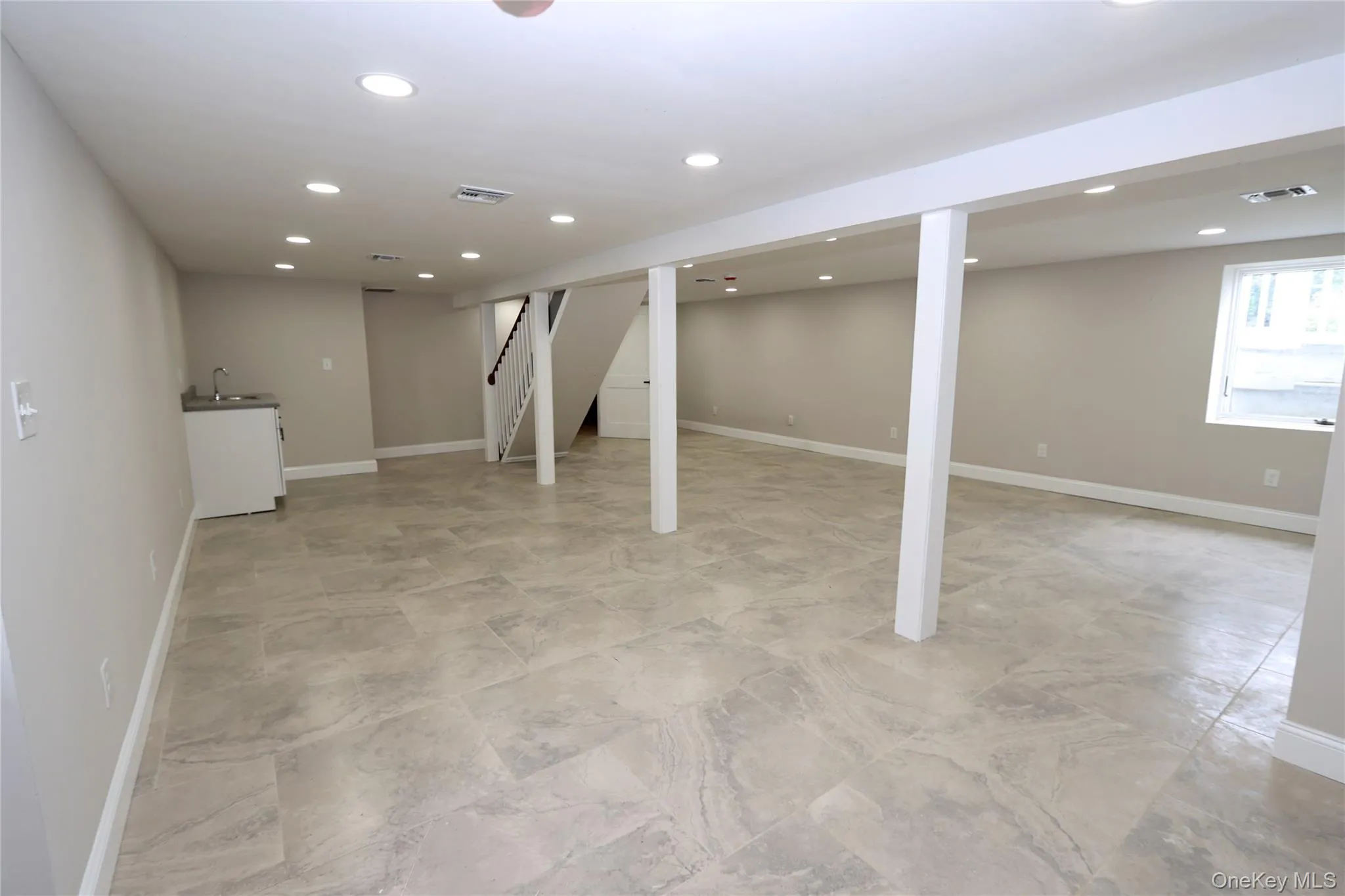 Spacious room featuring light-toned tile flooring, recessed lighting, and a utility sink with cabinetry Spacious room featuring light-toned tile flooring, recessed lighting, and a utility sink with cabinetry