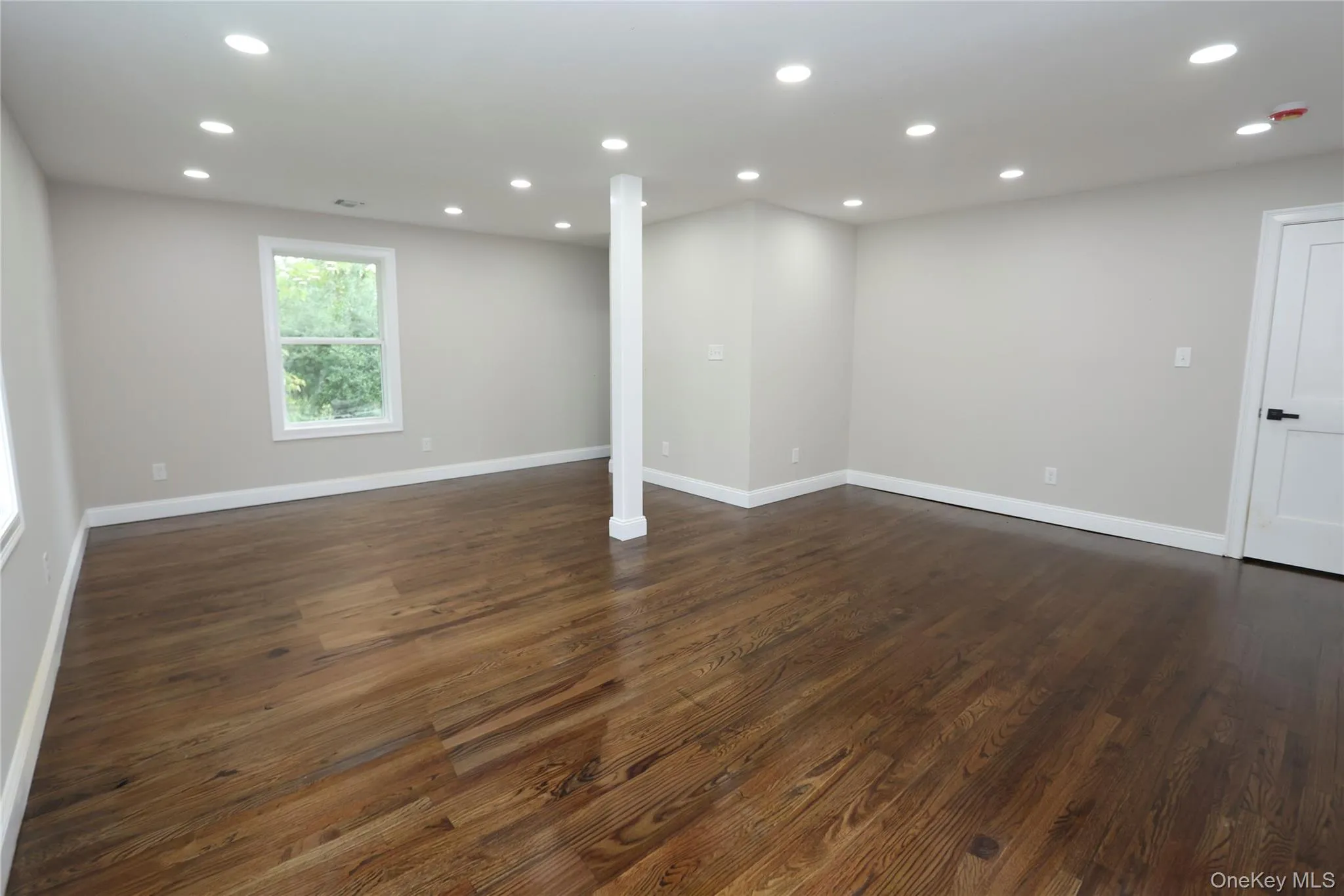 Spacious room with wood-finish flooring, recessed lighting, and a white paneled door with black hardware Spacious room with wood-finish flooring, recessed lighting, and a white paneled door with black hardware