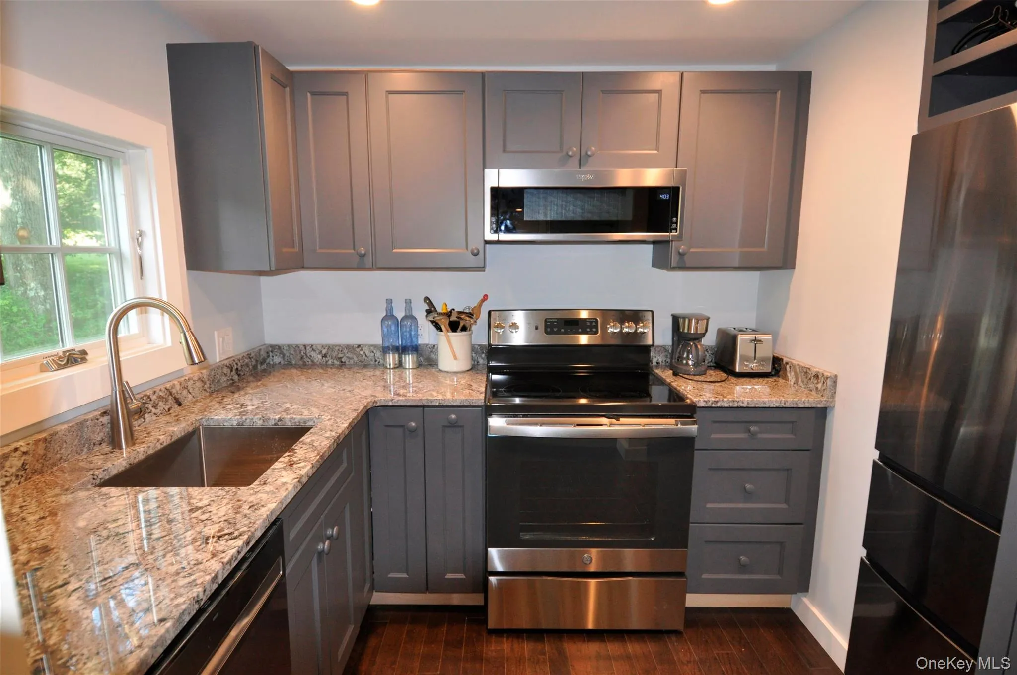 Kitchen featuring a sink, dark wood-style floors, gray cabinetry, light stone countertops, and stainless steel appliances Kitchen featuring a sink, dark wood-style floors, gray cabinetry, light stone countertops, and stainless steel appliances