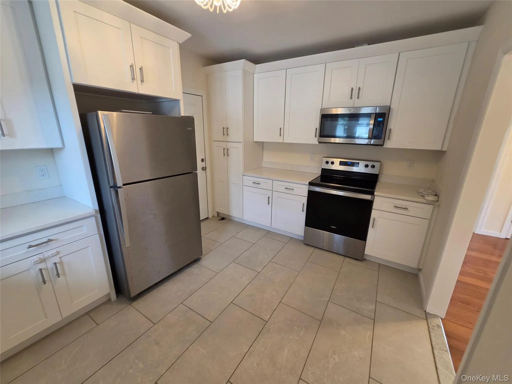 Kitchen featuring white shaker-style cabinetry, stainless steel appliances, solid surface countertops, and tile flooring Kitchen featuring white shaker-style cabinetry, stainless steel appliances, solid surface countertops, and tile flooring