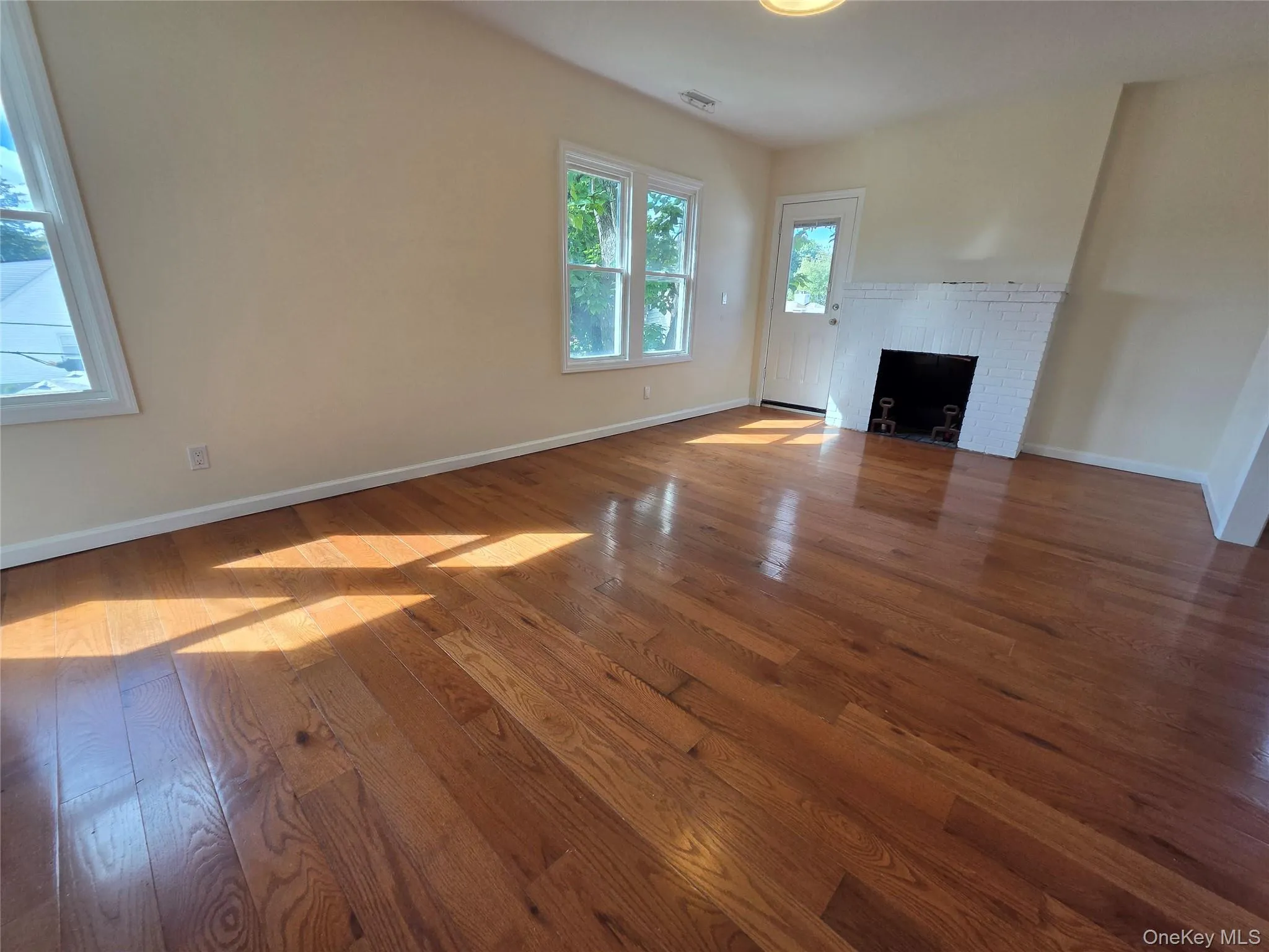 Wood-finish flooring, white trim, recessed fireplace, and multiple windows Wood-finish flooring, white trim, recessed fireplace, and multiple windows