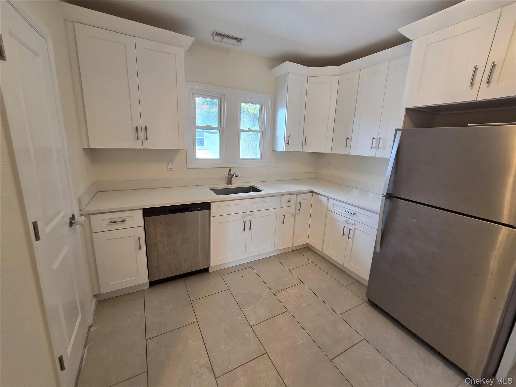 Kitchen featuring white shaker cabinetry, light-toned countertops, stainless steel appliances, and large format floor tiles Kitchen featuring white shaker cabinetry, light-toned countertops, stainless steel appliances, and large format floor tiles