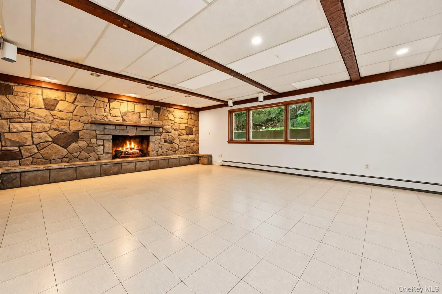 Lower level family room has stone fireplace and beamed ceiling with large windows and acoustic ceiling. Extraneous objects removed. Lower level family room has stone fireplace and beamed ceiling with large windows and acoustic ceiling. Extraneous objects removed.