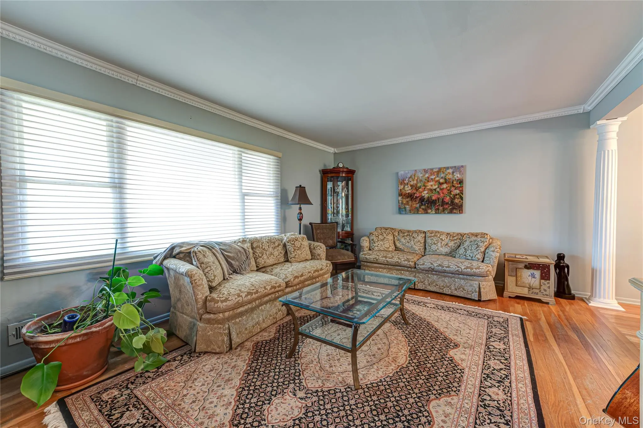 Hardwood flooring, crown molding, a large picture window with blinds, and decorative fluted columns Hardwood flooring, crown molding, a large picture window with blinds, and decorative fluted columns
