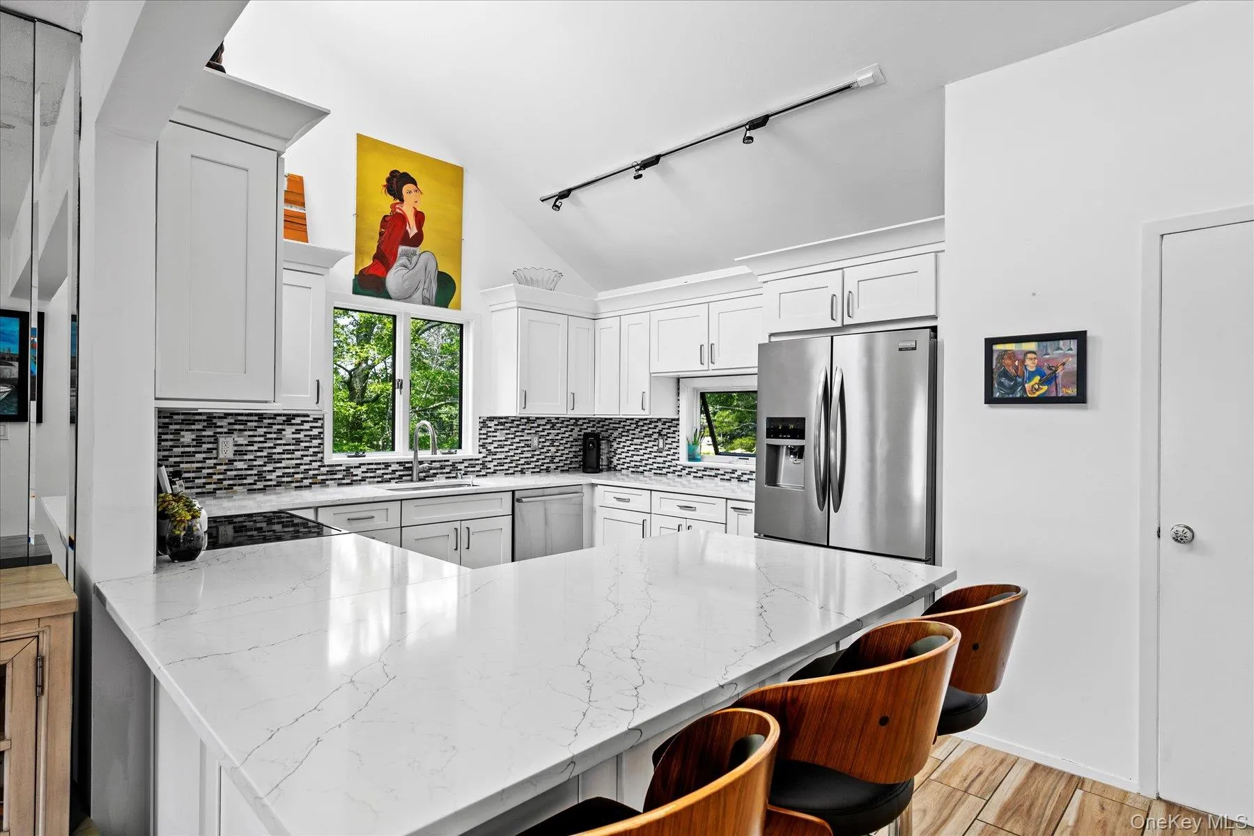 Kitchen featuring a peninsula, lofted ceiling, rail lighting, light stone countertops, and a breakfast bar Kitchen featuring a peninsula, lofted ceiling, rail lighting, light stone countertops, and a breakfast bar