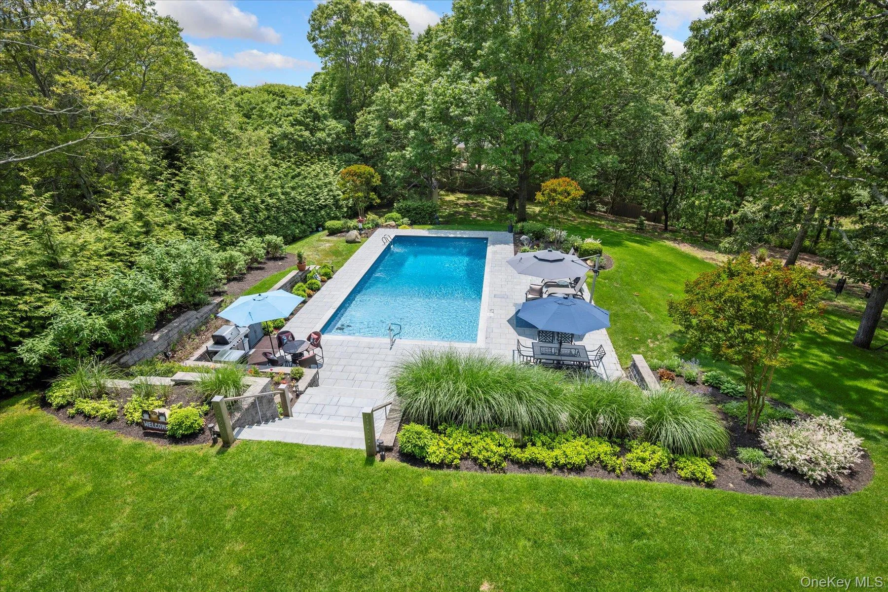 Outdoor pool with a lawn, a patio area, and a wooded view Outdoor pool with a lawn, a patio area, and a wooded view