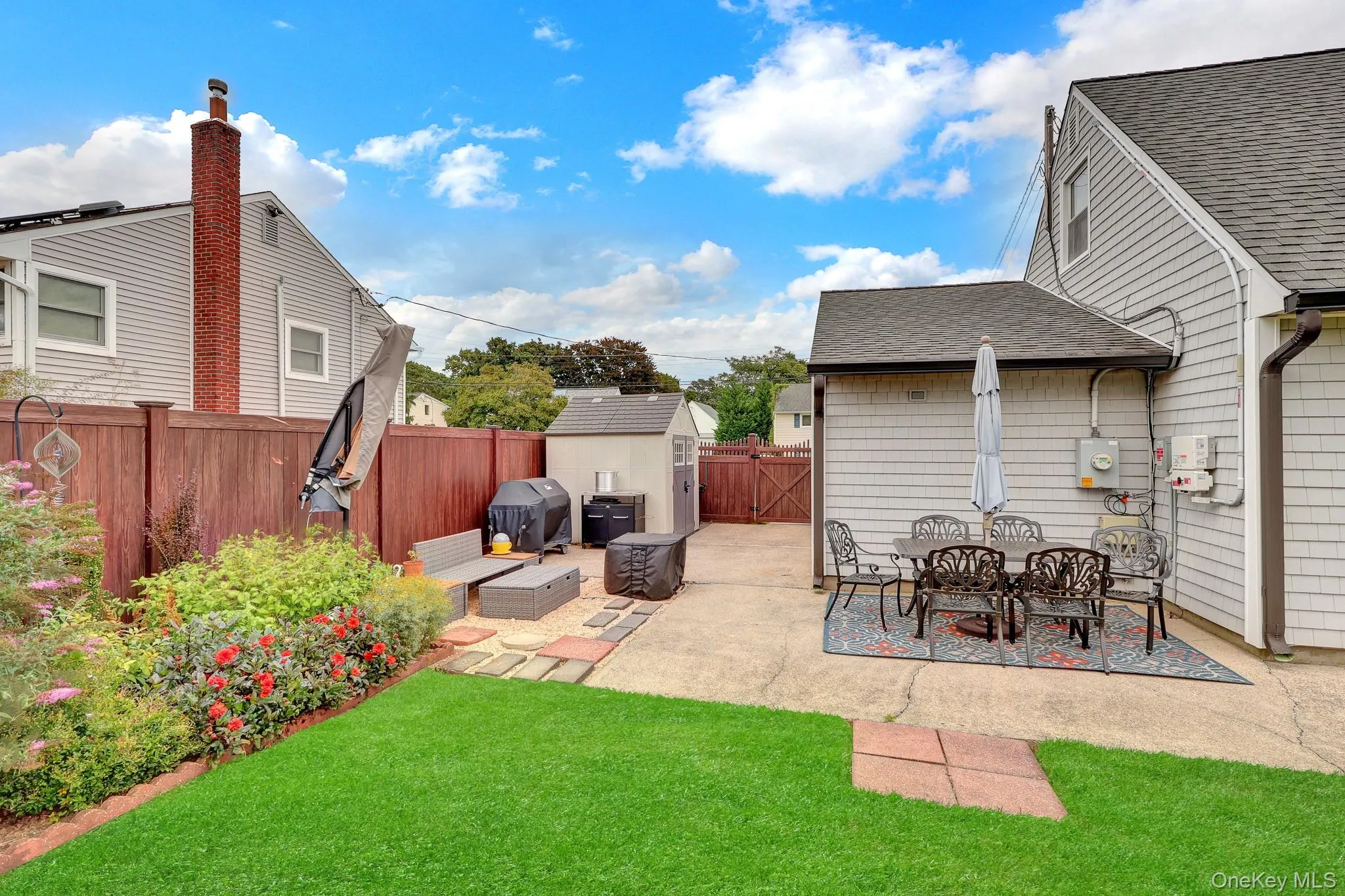 Expansive backyard oasis featuring a manicured lawn, brick paver patio with dining area, mature landscaping with flowering shrubs, and a detached storage structure Expansive backyard oasis featuring a manicured lawn, brick paver patio with dining area, mature landscaping with flowering shrubs, and a detached storage structure