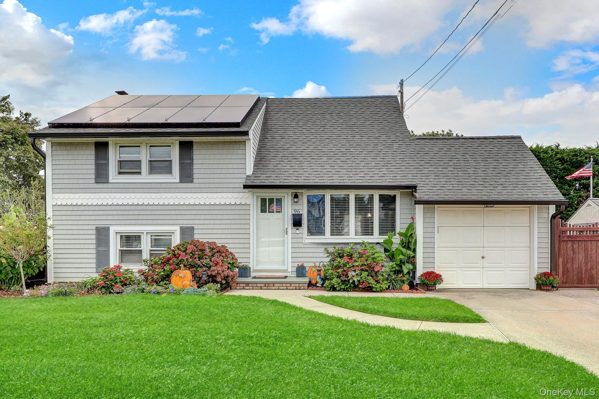 Light gray siding exterior with dark gray functional shutters, solar panels, and a single-car garage Light gray siding exterior with dark gray functional shutters, solar panels, and a single-car garage