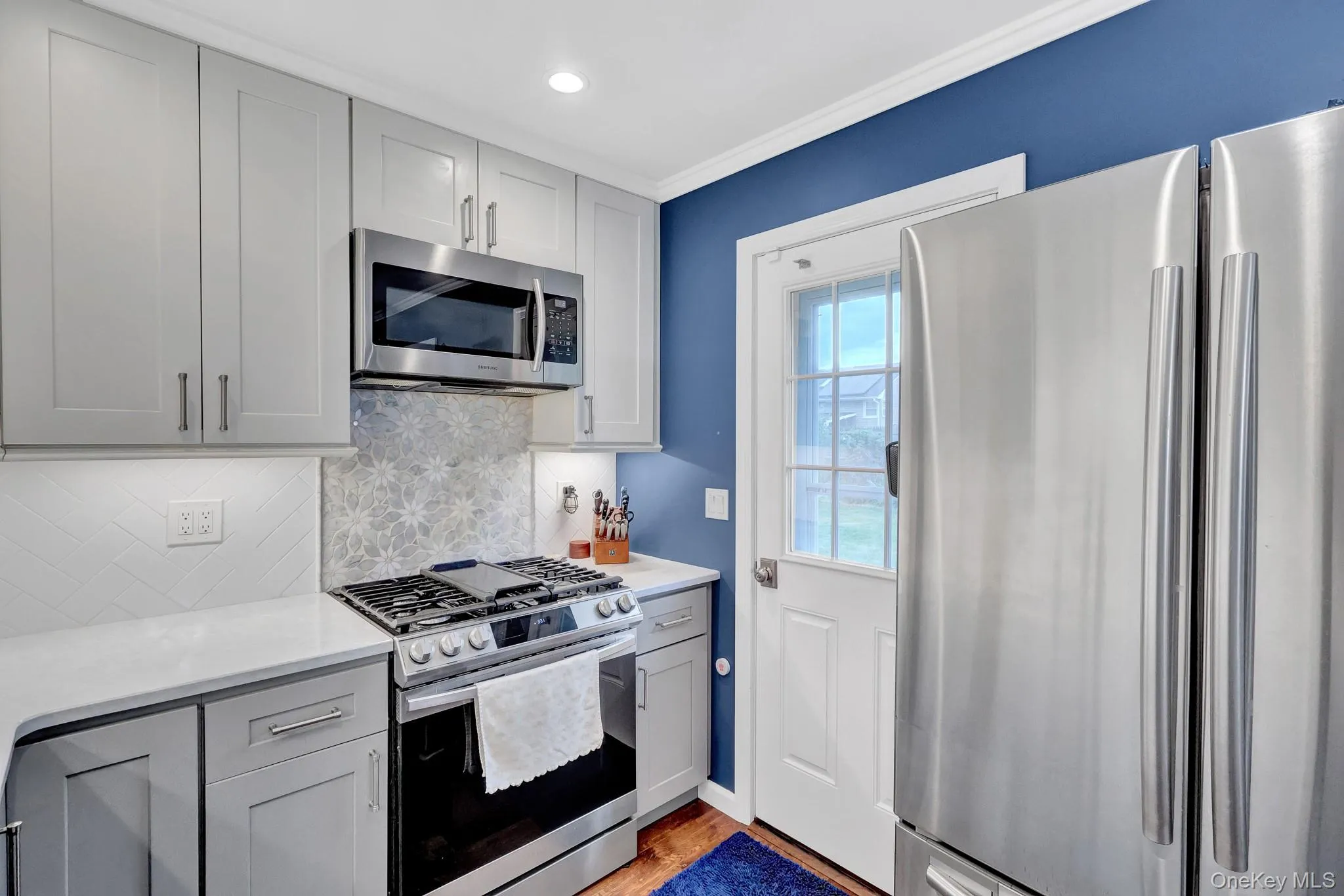 Stainless steel appliances, light gray cabinetry, white countertops, decorative tile backsplash, and a white paneled door Stainless steel appliances, light gray cabinetry, white countertops, decorative tile backsplash, and a white paneled door