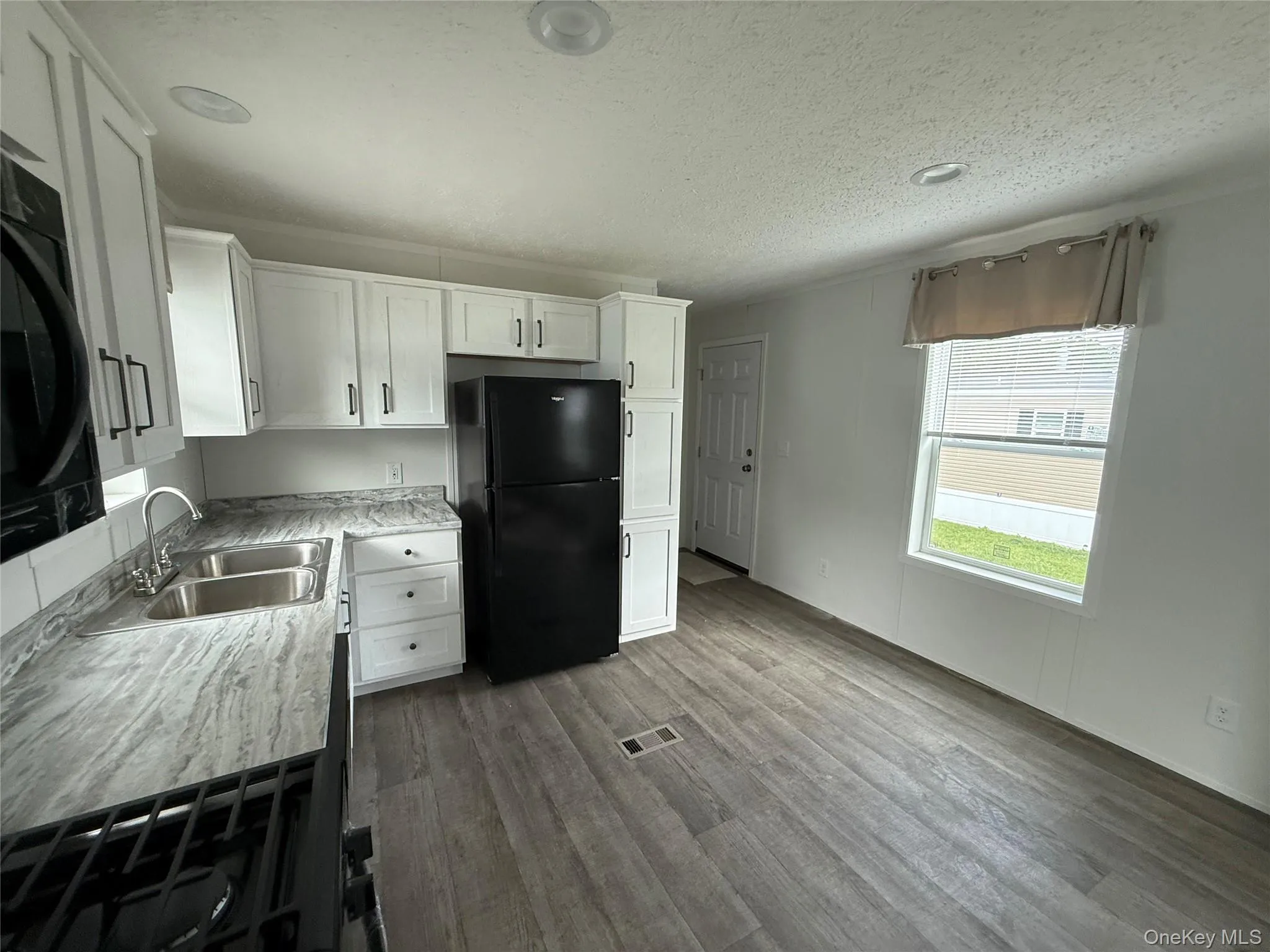 Kitchen with white cabinets, black appliances, light countertops, dark wood-type flooring, and a textured ceiling Kitchen with white cabinets, black appliances, light countertops, dark wood-type flooring, and a textured ceiling