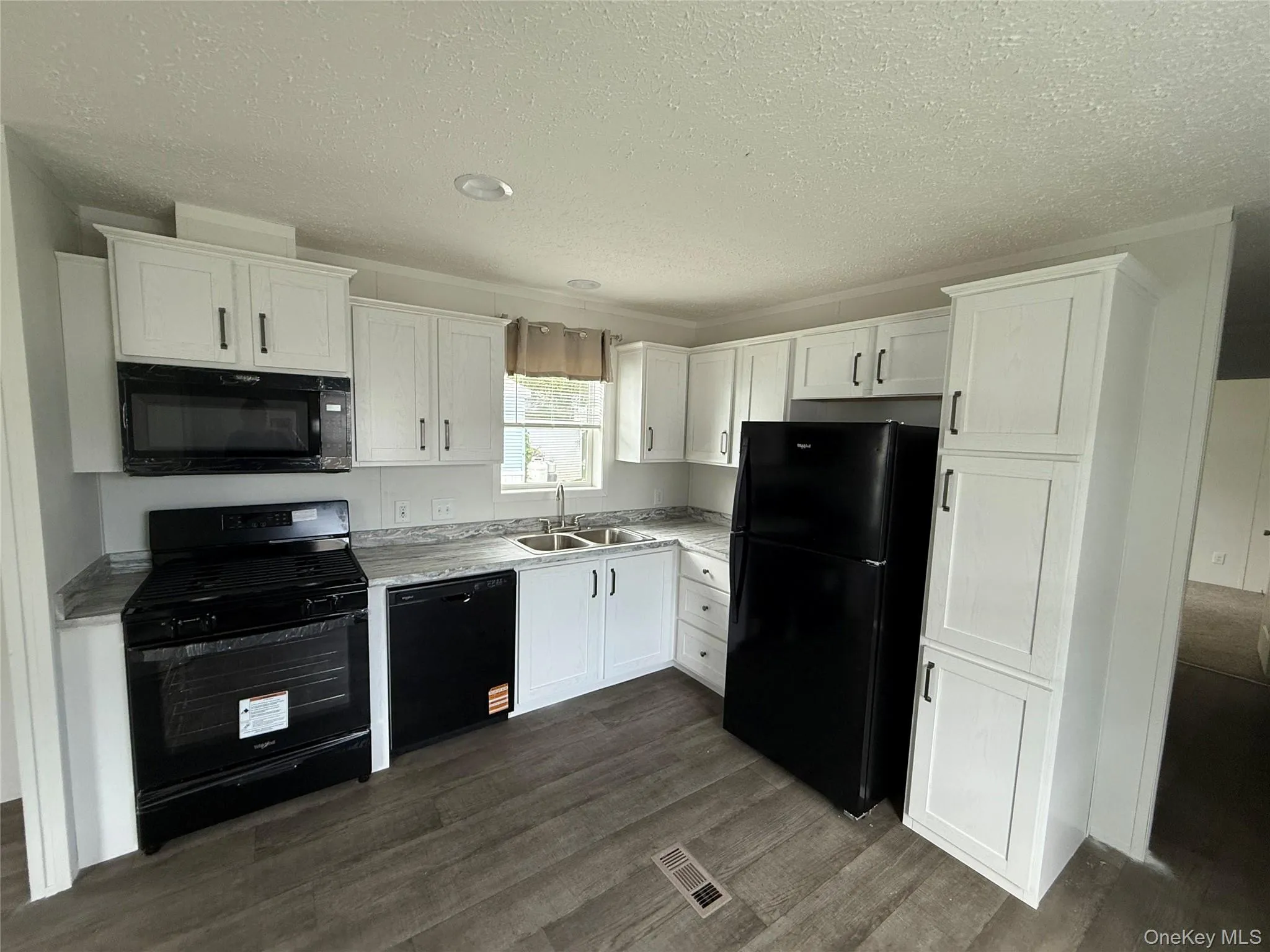 Kitchen with black appliances, white cabinetry, a textured ceiling, dark wood finished floors, and light countertops Kitchen with black appliances, white cabinetry, a textured ceiling, dark wood finished floors, and light countertops