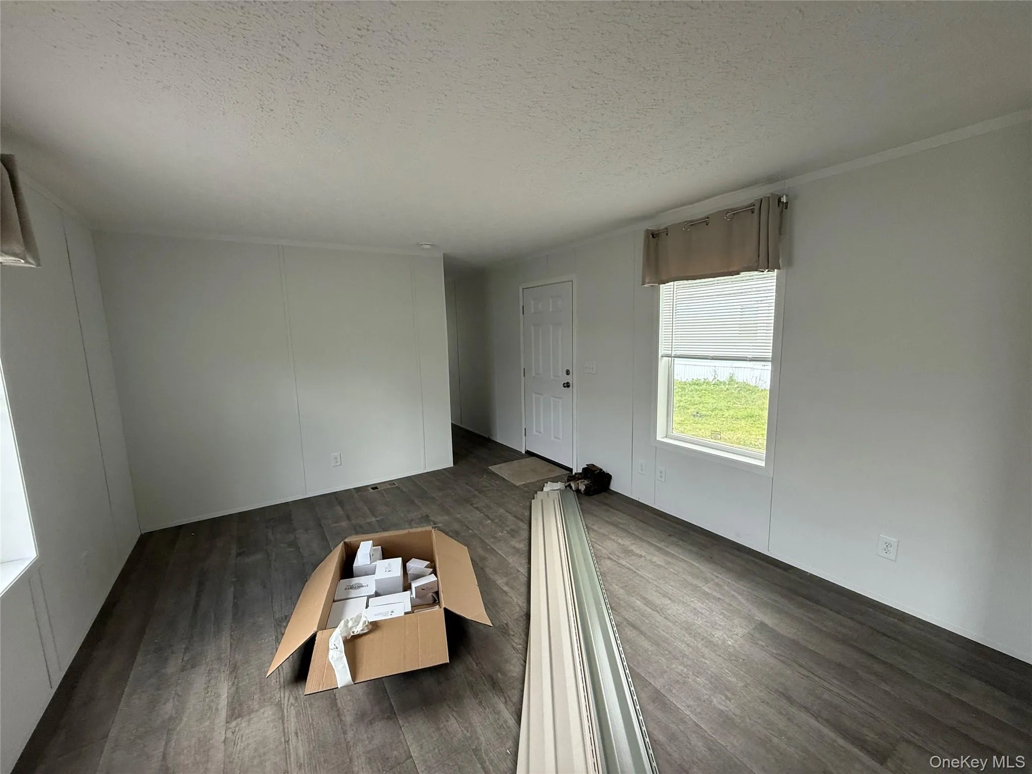 Unfurnished living room with a textured ceiling, dark wood-type flooring, and ornamental molding Unfurnished living room with a textured ceiling, dark wood-type flooring, and ornamental molding