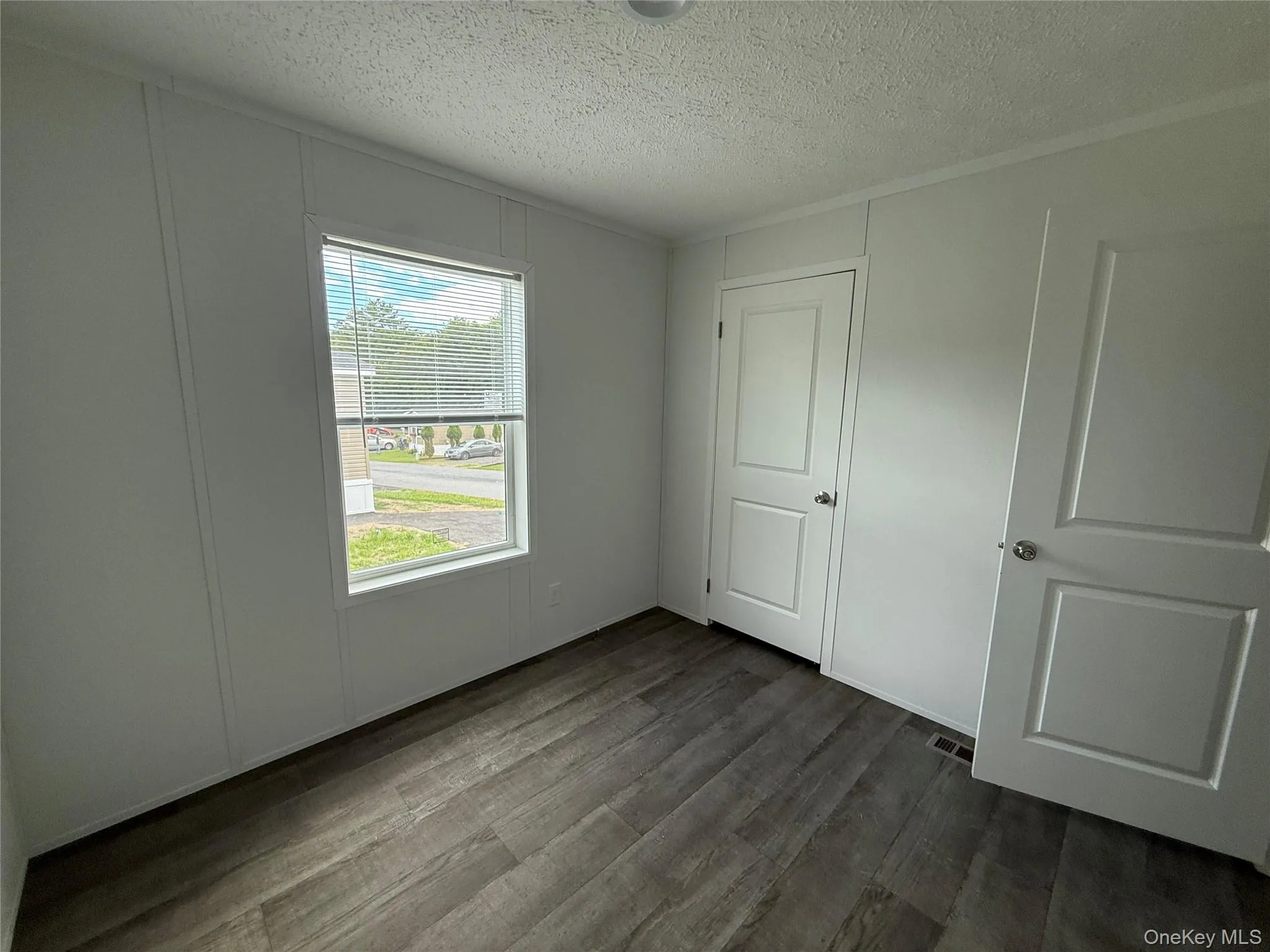 Unfurnished bedroom featuring dark wood-type flooring, a textured ceiling, and a closet Unfurnished bedroom featuring dark wood-type flooring, a textured ceiling, and a closet