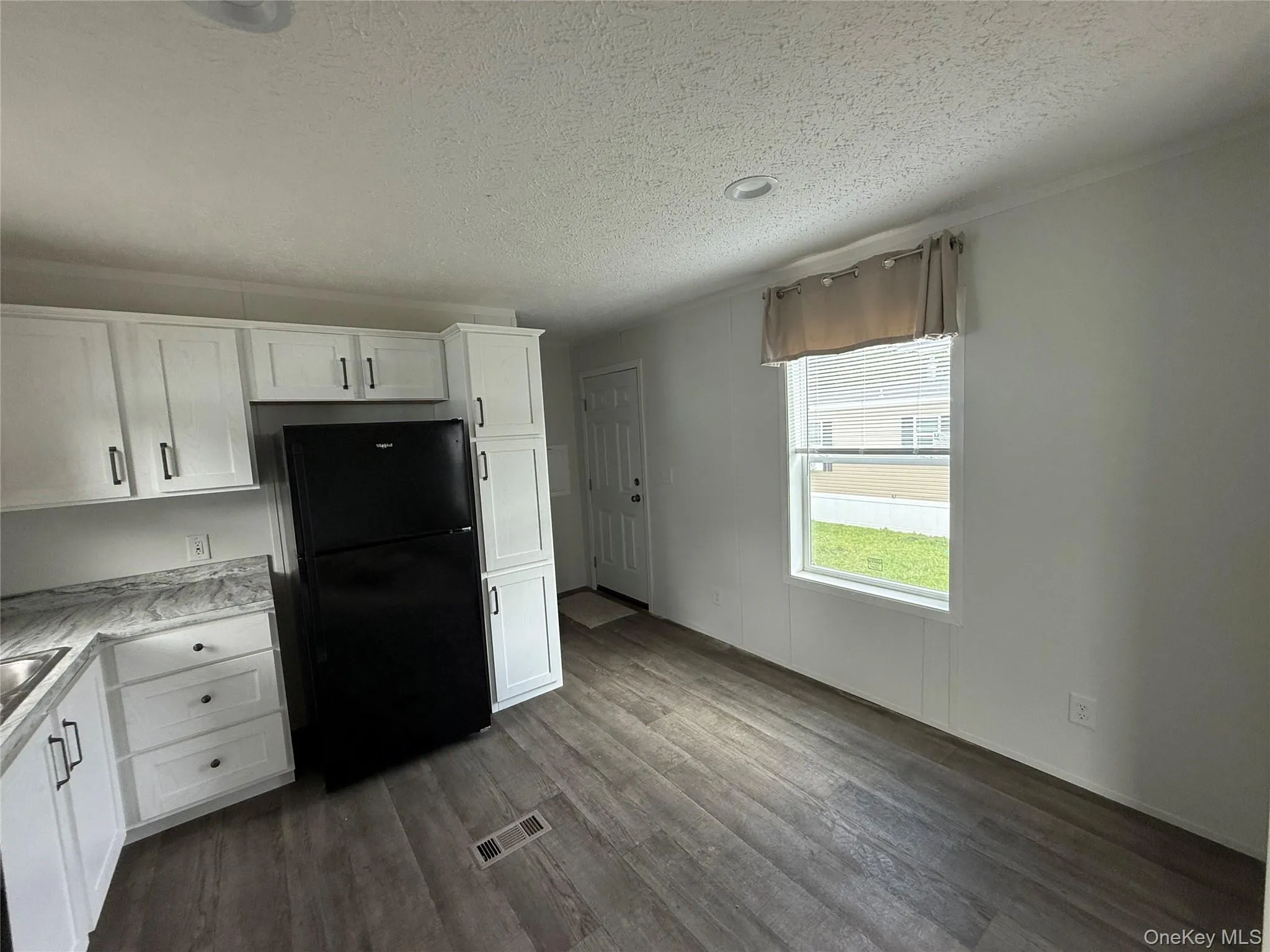Kitchen featuring white cabinets, freestanding refrigerator, dark wood-type flooring, and a textured ceiling Kitchen featuring white cabinets, freestanding refrigerator, dark wood-type flooring, and a textured ceiling