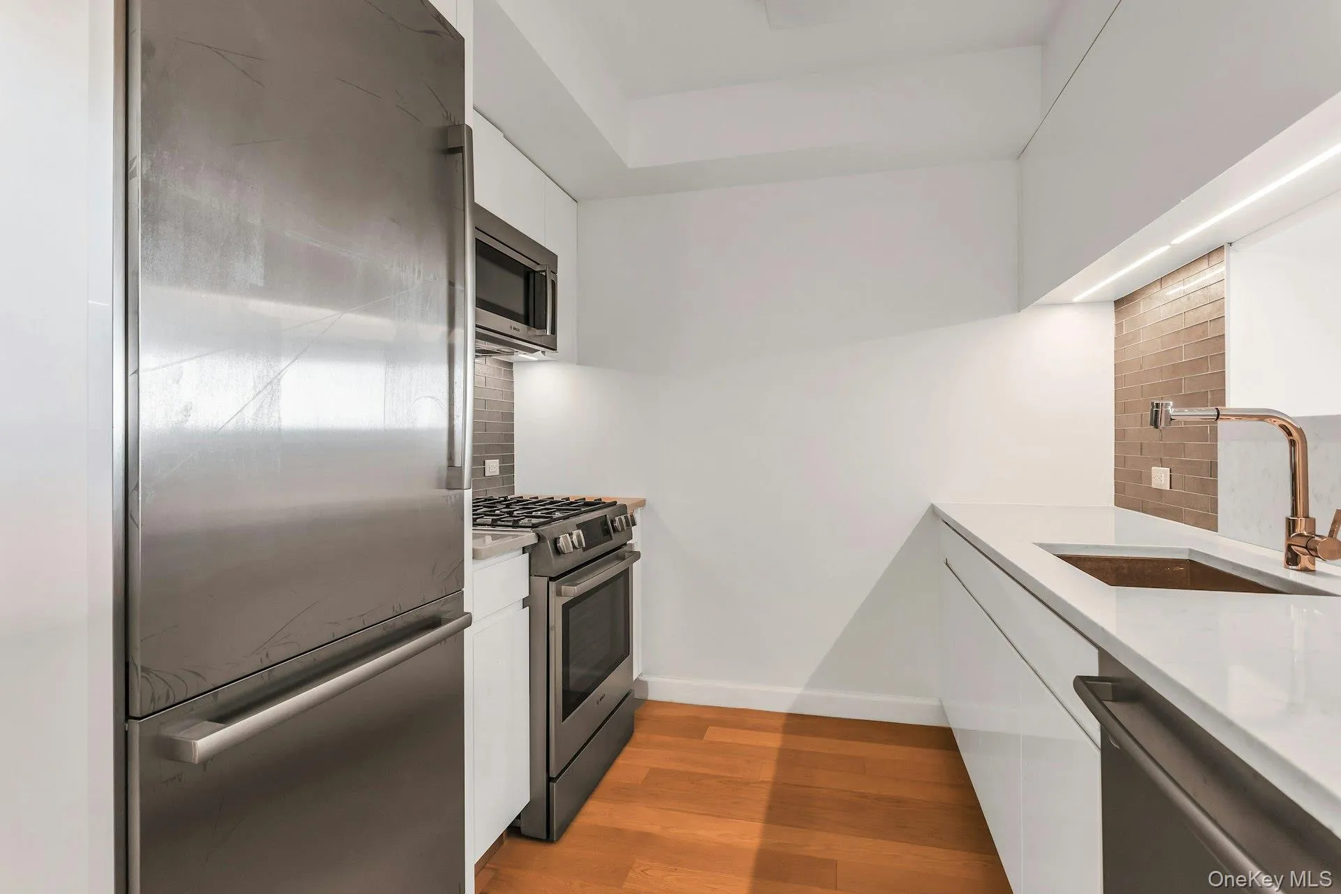Kitchen with white cabinets, stainless steel appliances, light stone counters, and dark wood-style floors Kitchen with white cabinets, stainless steel appliances, light stone counters, and dark wood-style floors