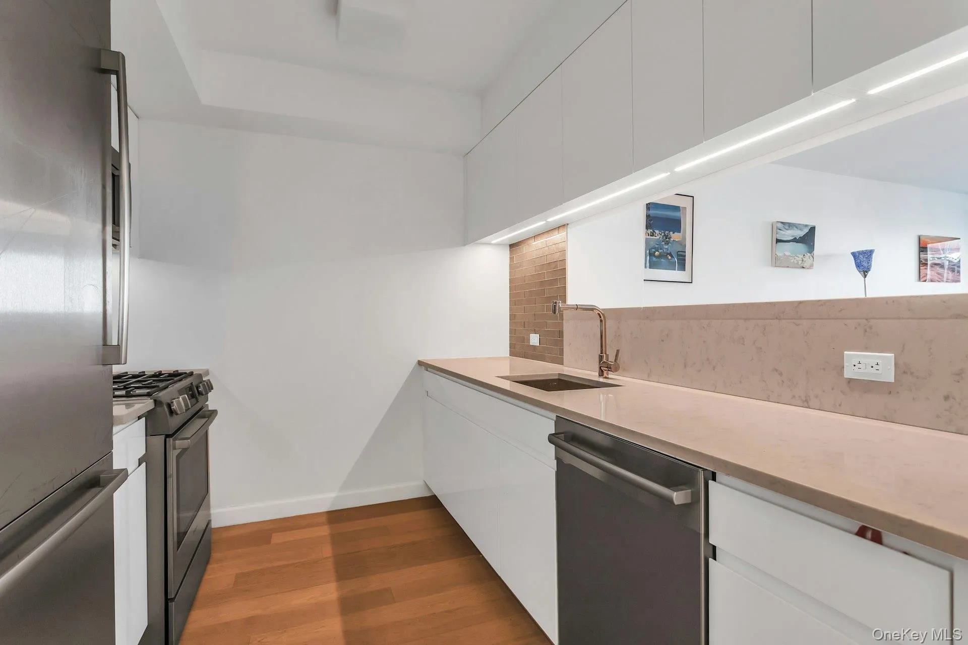 Kitchen featuring white cabinetry, appliances with stainless steel finishes, decorative backsplash, light stone countertops, and modern cabinets Kitchen featuring white cabinetry, appliances with stainless steel finishes, decorative backsplash, light stone countertops, and modern cabinets
