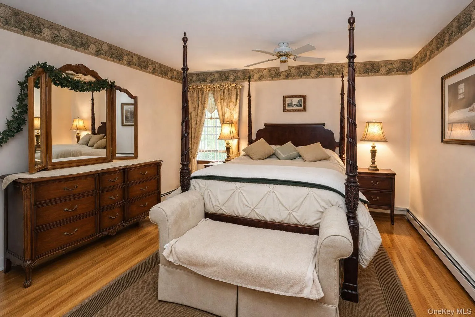 Wood-finish flooring, ceiling fan with integrated lighting, window with decorative drapery, and a classic dresser with an attached mirror Wood-finish flooring, ceiling fan with integrated lighting, window with decorative drapery, and a classic dresser with an attached mirror