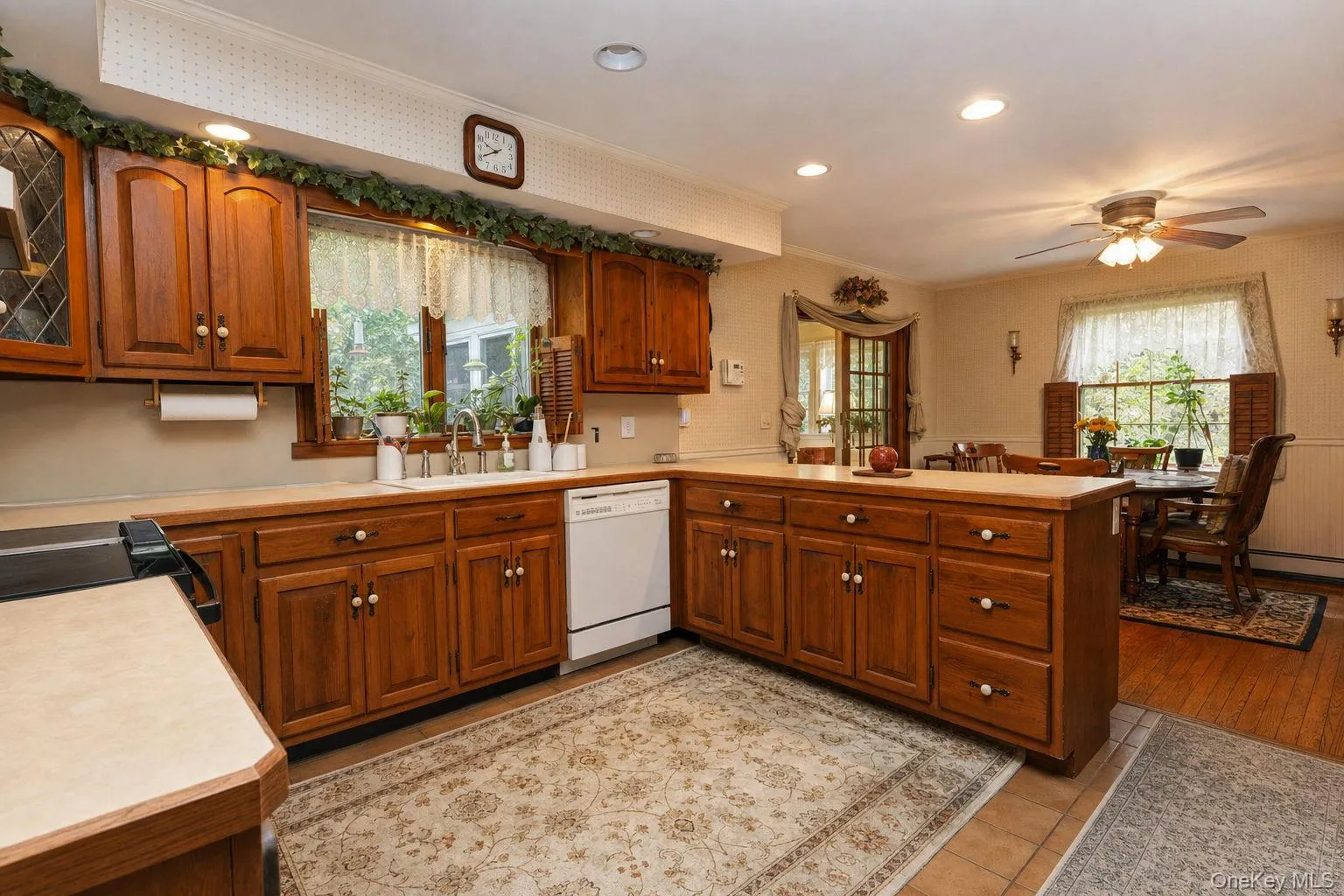 Kitchen featuring wood cabinetry with pullout shelving, solid surface countertops, recessed lighting, and a dining area with a ceiling fan Kitchen featuring wood cabinetry with pullout shelving, solid surface countertops, recessed lighting, and a dining area with a ceiling fan